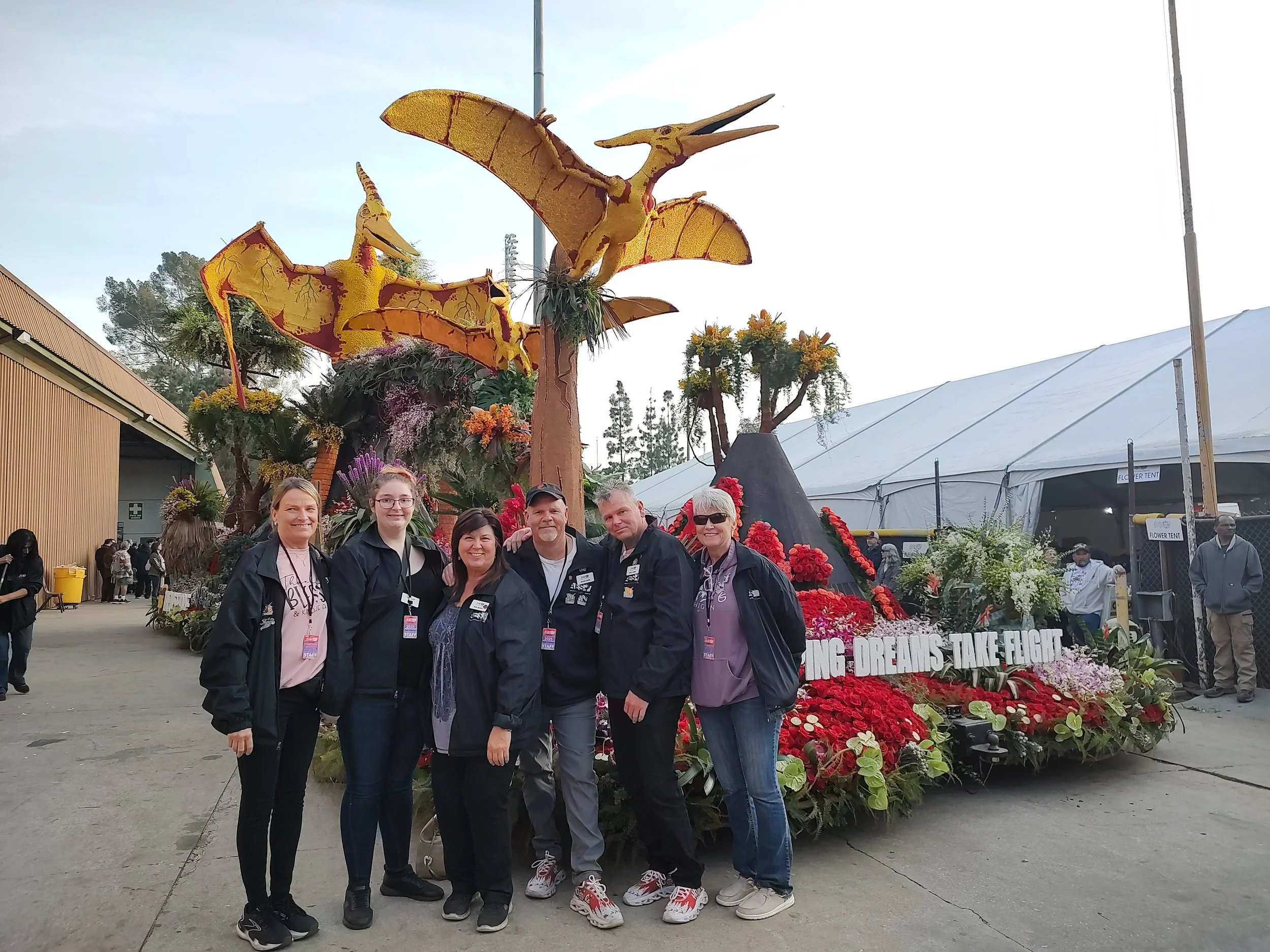 Group of people smiling and standing in front of a large floral display with statues of dragons and flowers in the background.