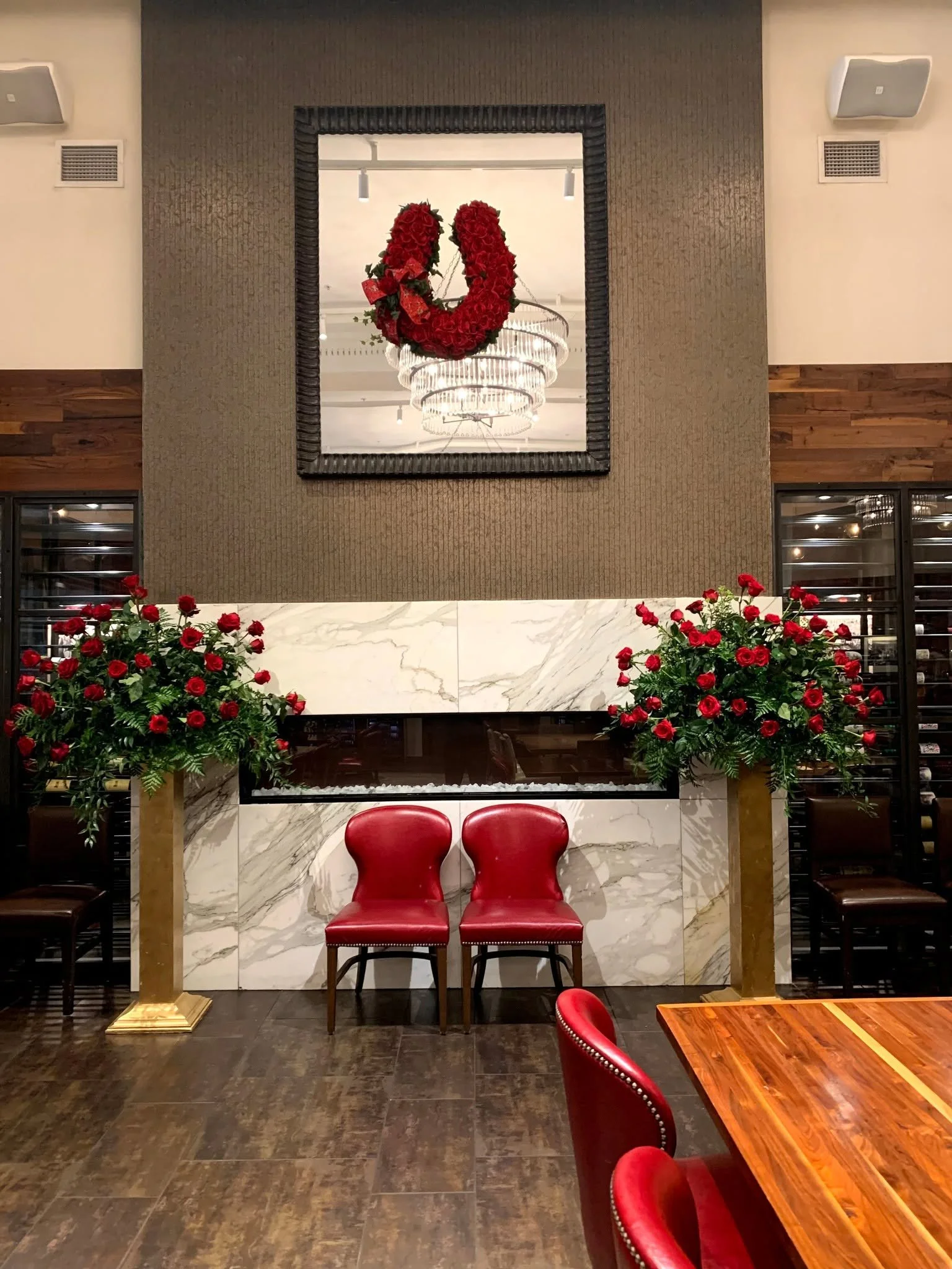 Decorative interior with a large mirror, red roses in pots, and red chairs.