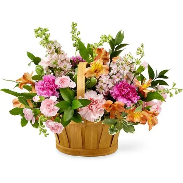 A wooden basket filled with pink, orange, and white flowers, including carnations and lilies, with green foliage.