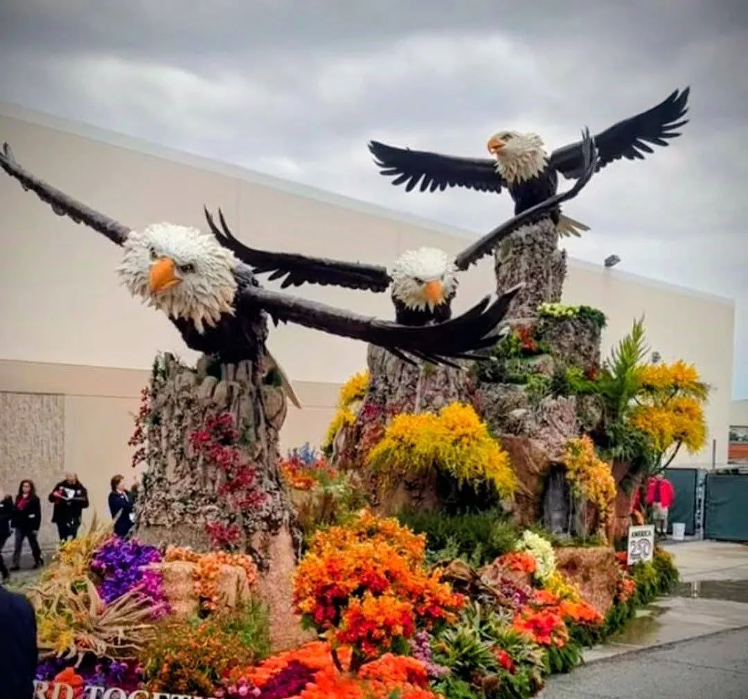 Large decorative display of three bald eagles with outstretched wings atop rocky structures, surrounded by colorful autumn flowers and foliage.