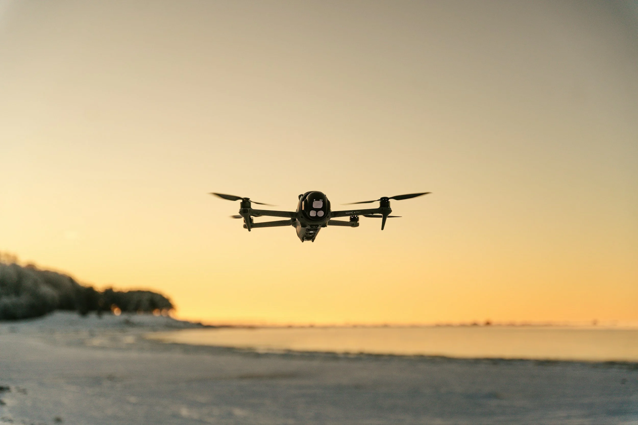 A drone flying over a beach during sunset with a blurred shoreline in the foreground.