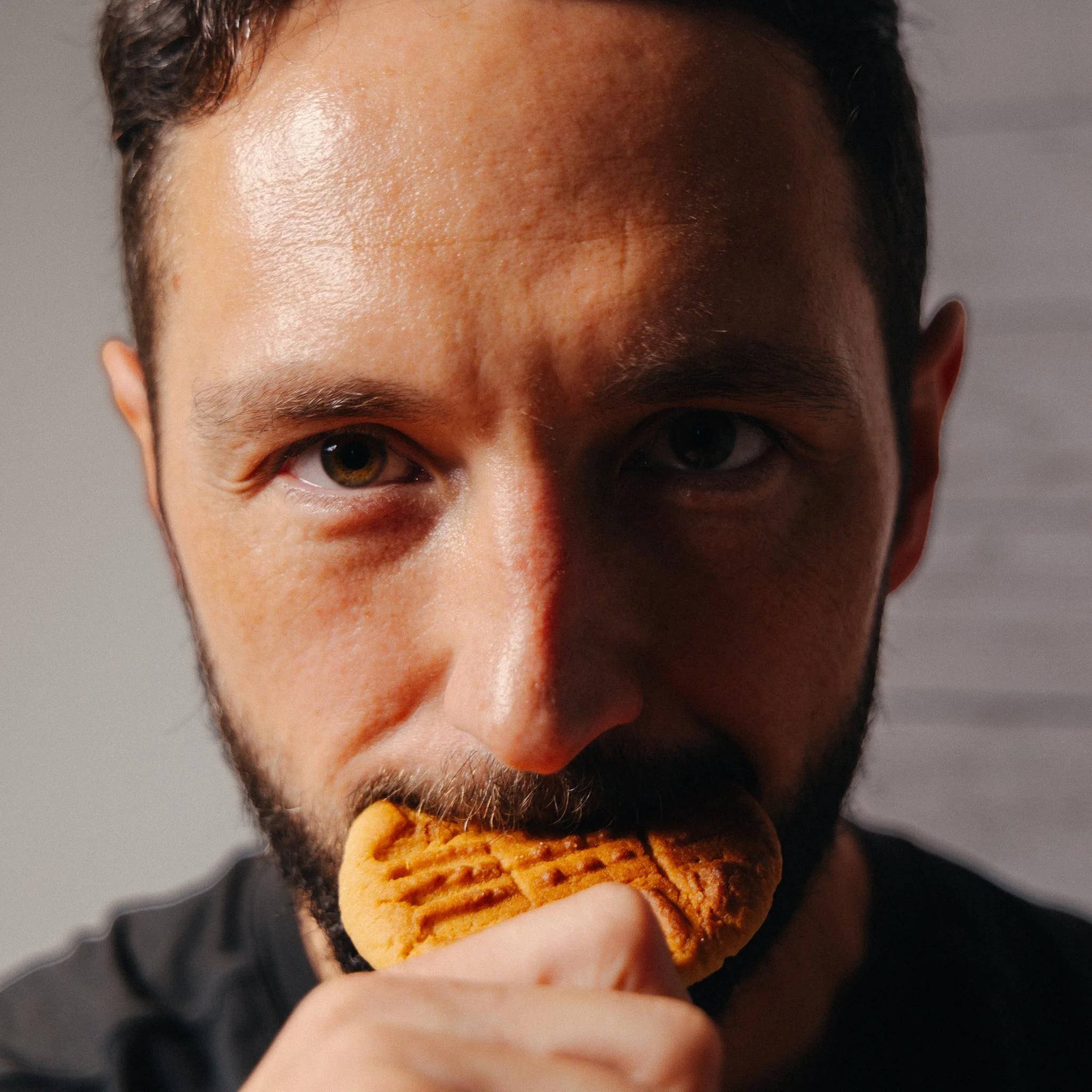A close-up of a person's face with a cookie near their mouth, with part of their forehead, eyes, and nose visible.