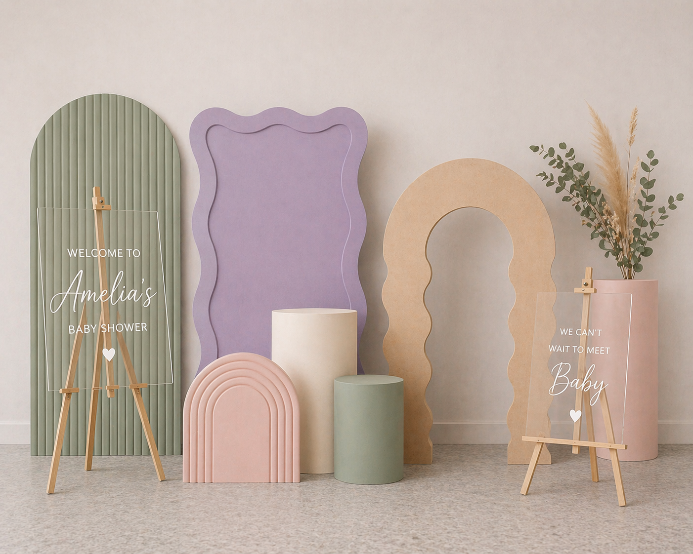 Decorative baby shower backdrop with pastel-colored panels, signs, and plants, welcoming guests to Amelia's baby shower with the message 'We can't wait to meet Baby' and a sign reading 'Welcome to Amelia's Baby Shower.'