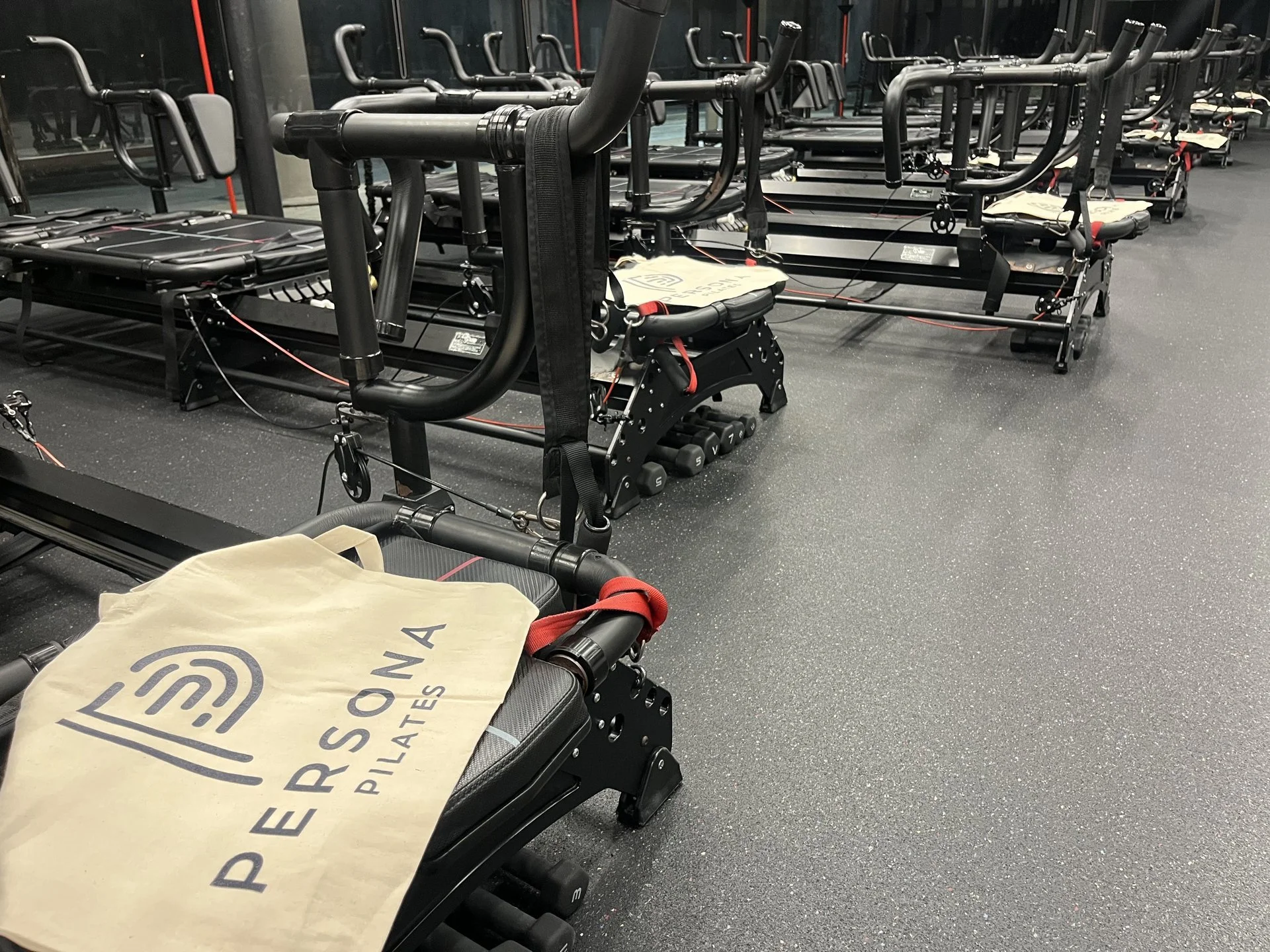 Empty Persona Pilates studio with a row of black Maven reformers and a welcome tote on the front carriage