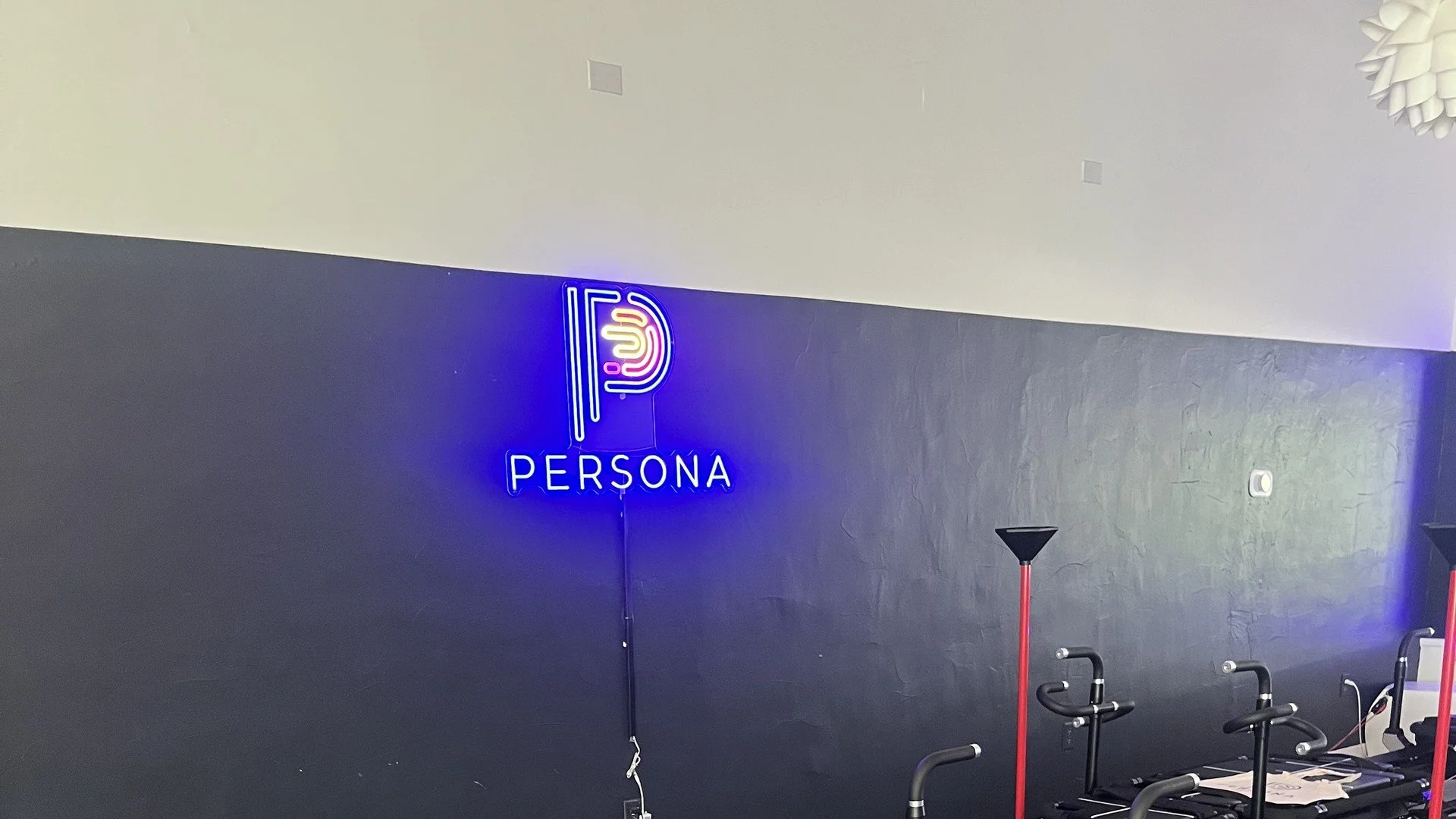 Empty Maven reformers under a neon Persona Pilates sign, with branded welcome totes on the front carriages