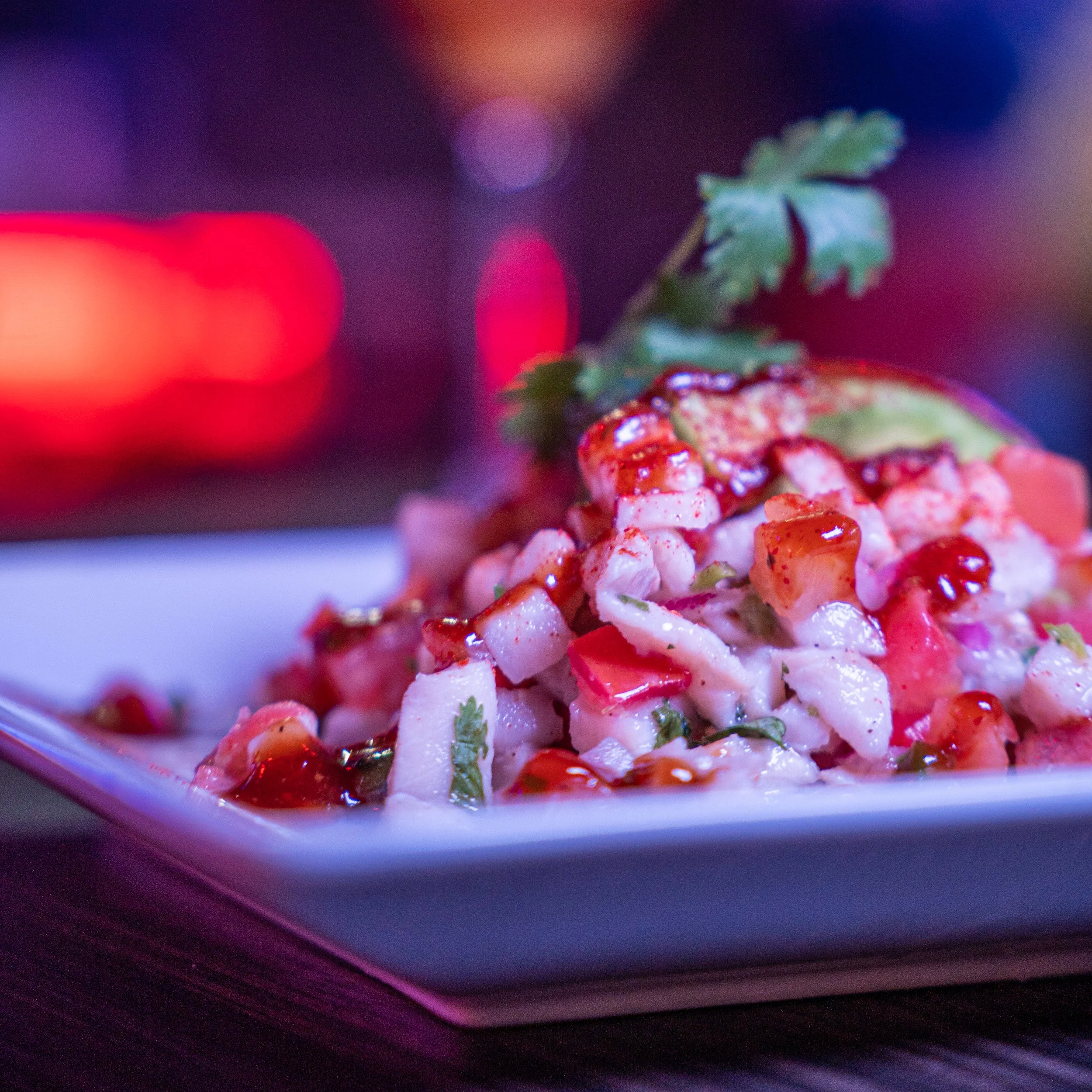 Close-up of a fruit salad with diced fruits and herbs on a white plate, with colorful bokeh lights in the background.