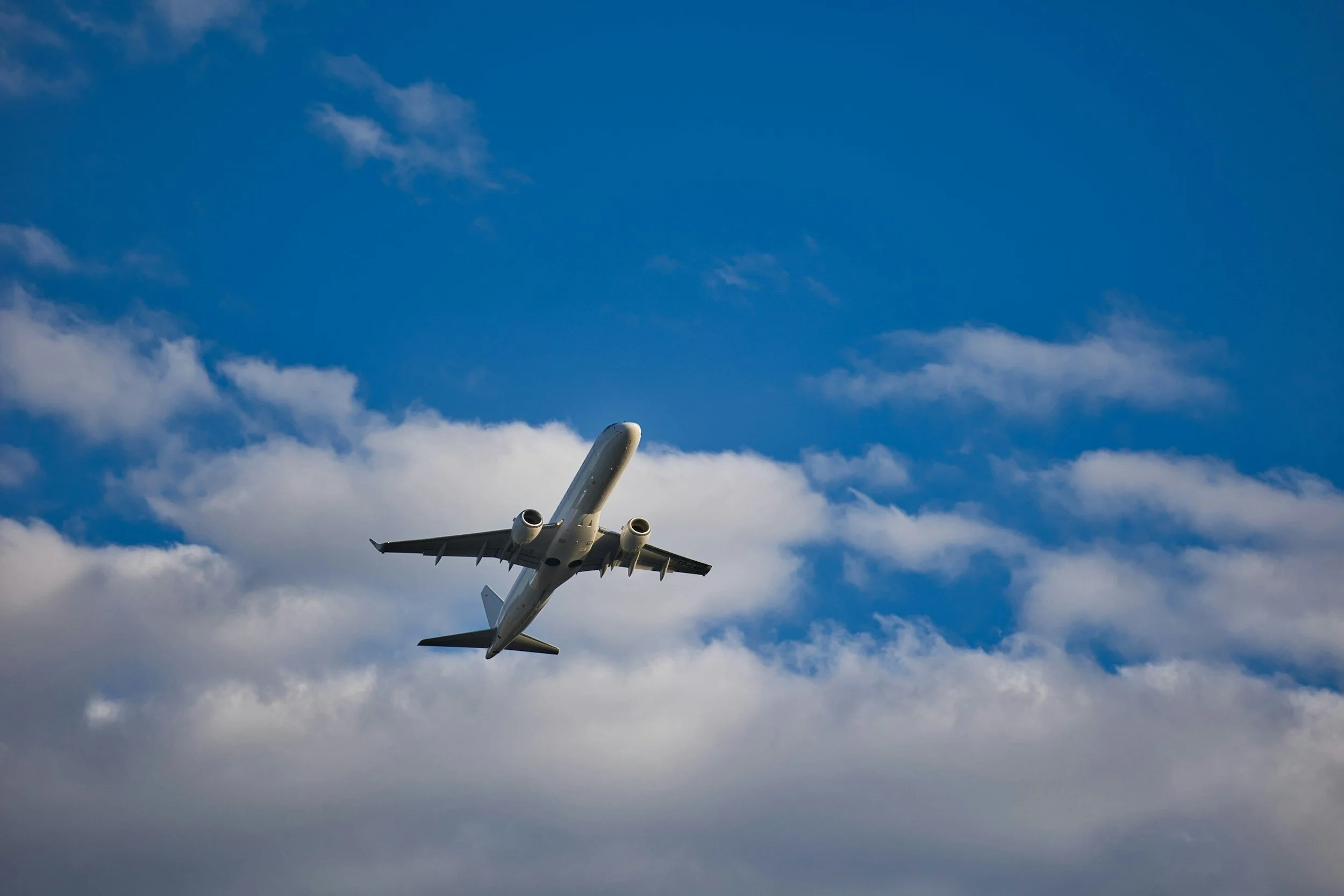 A commercial airplane flying in a cloudy blue sky, viewed from below.