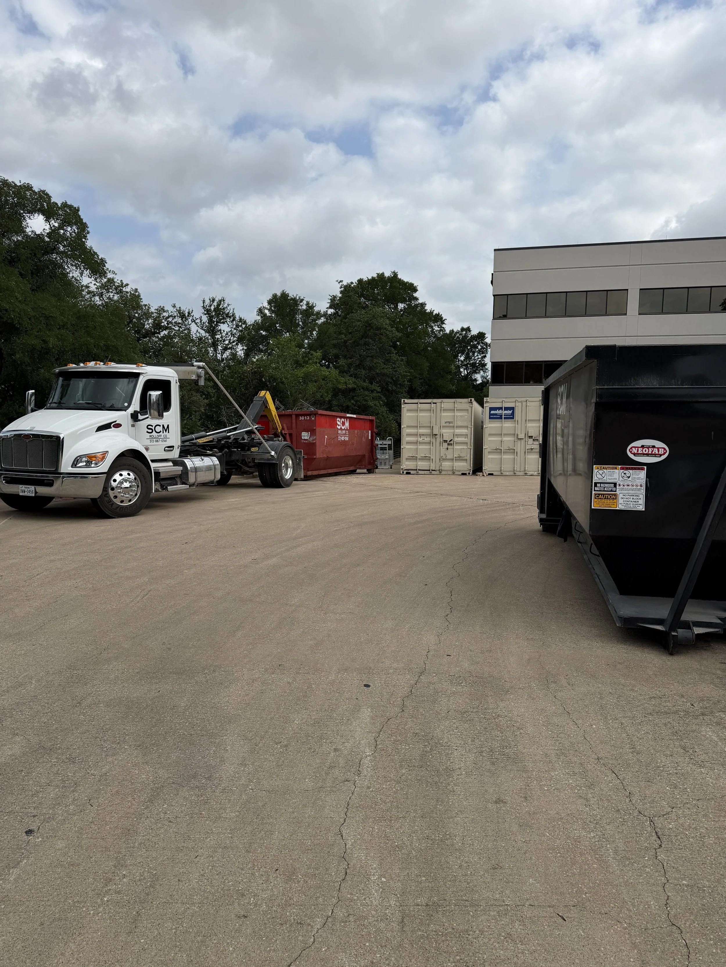 Parking lot with trucks, containers, and a building under a cloudy sky.