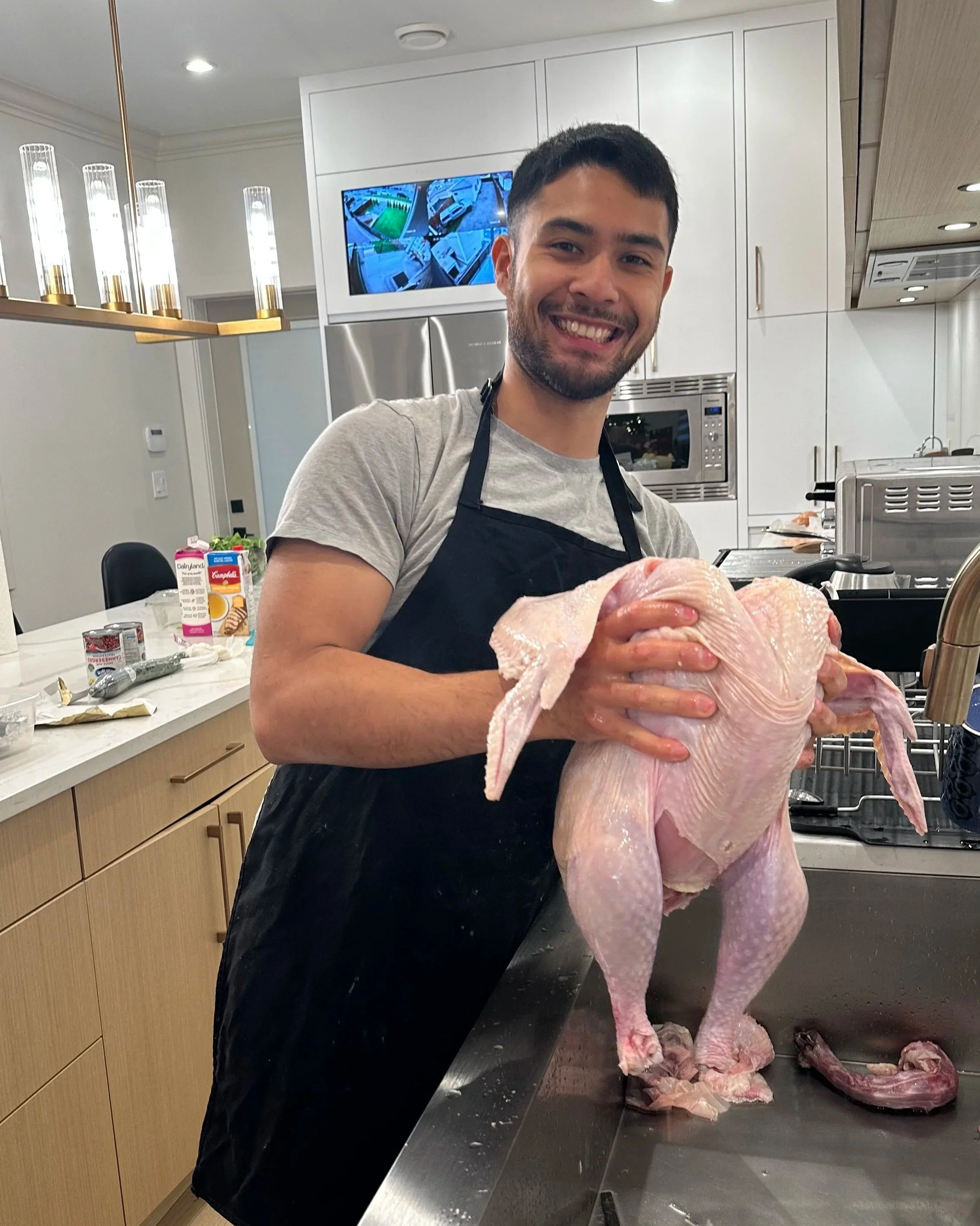 A man smiling and holding up a raw, whole turkey in a modern kitchen.