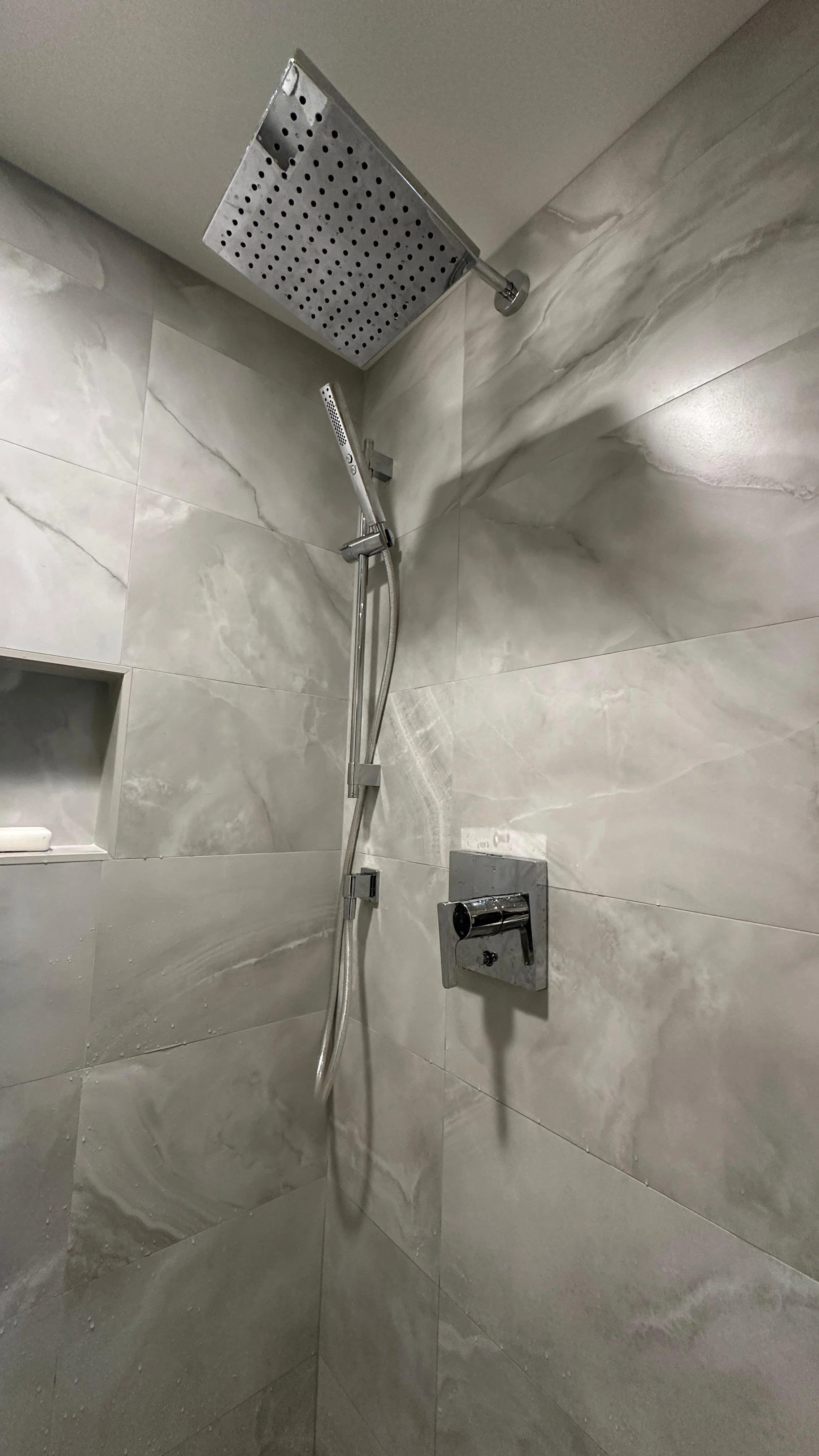 Shower with a large rain showerhead, a handheld showerhead, and a wall-mounted control.