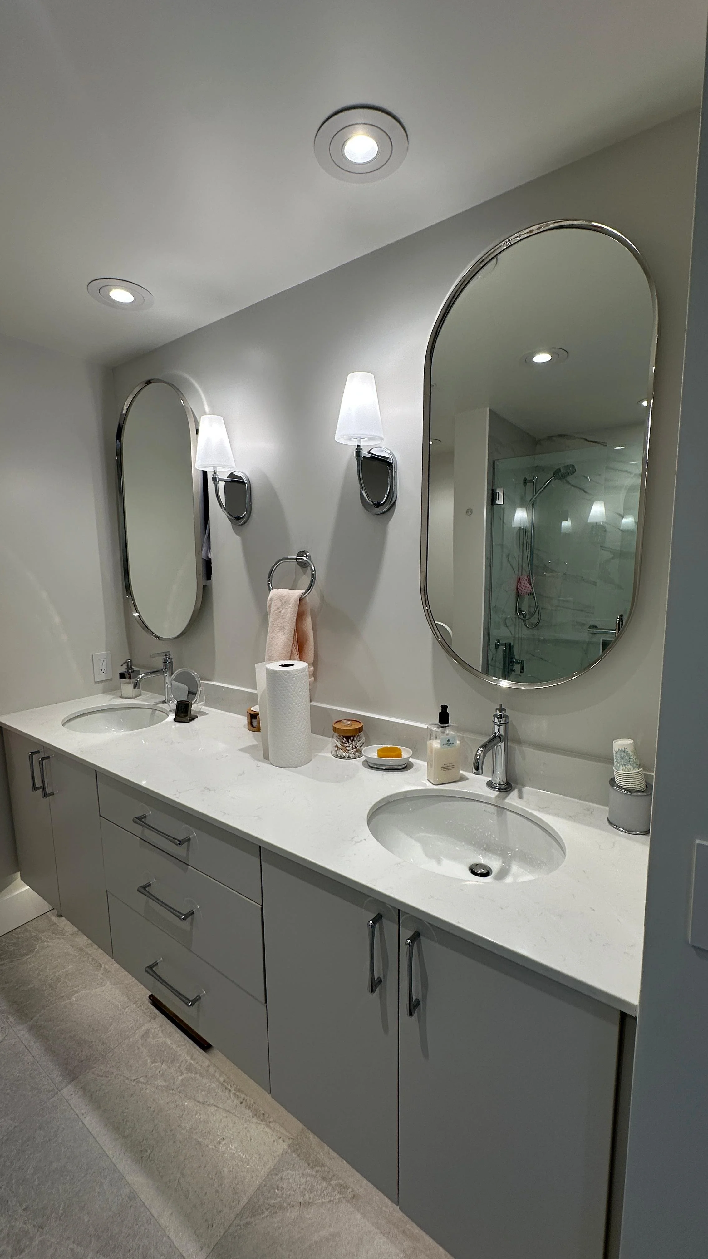 Bathroom vanity with two sinks, oval mirrors, wall sconces, and various toiletries on the countertop.