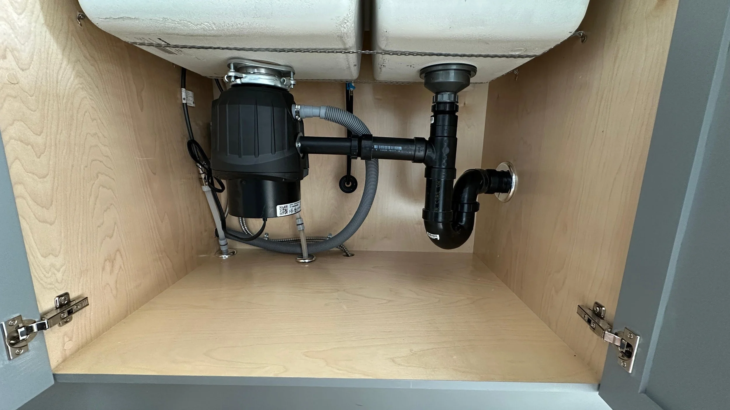 Under sink plumbing with a water filtration system, black pipes, and PVC fittings inside a wooden cabinet.