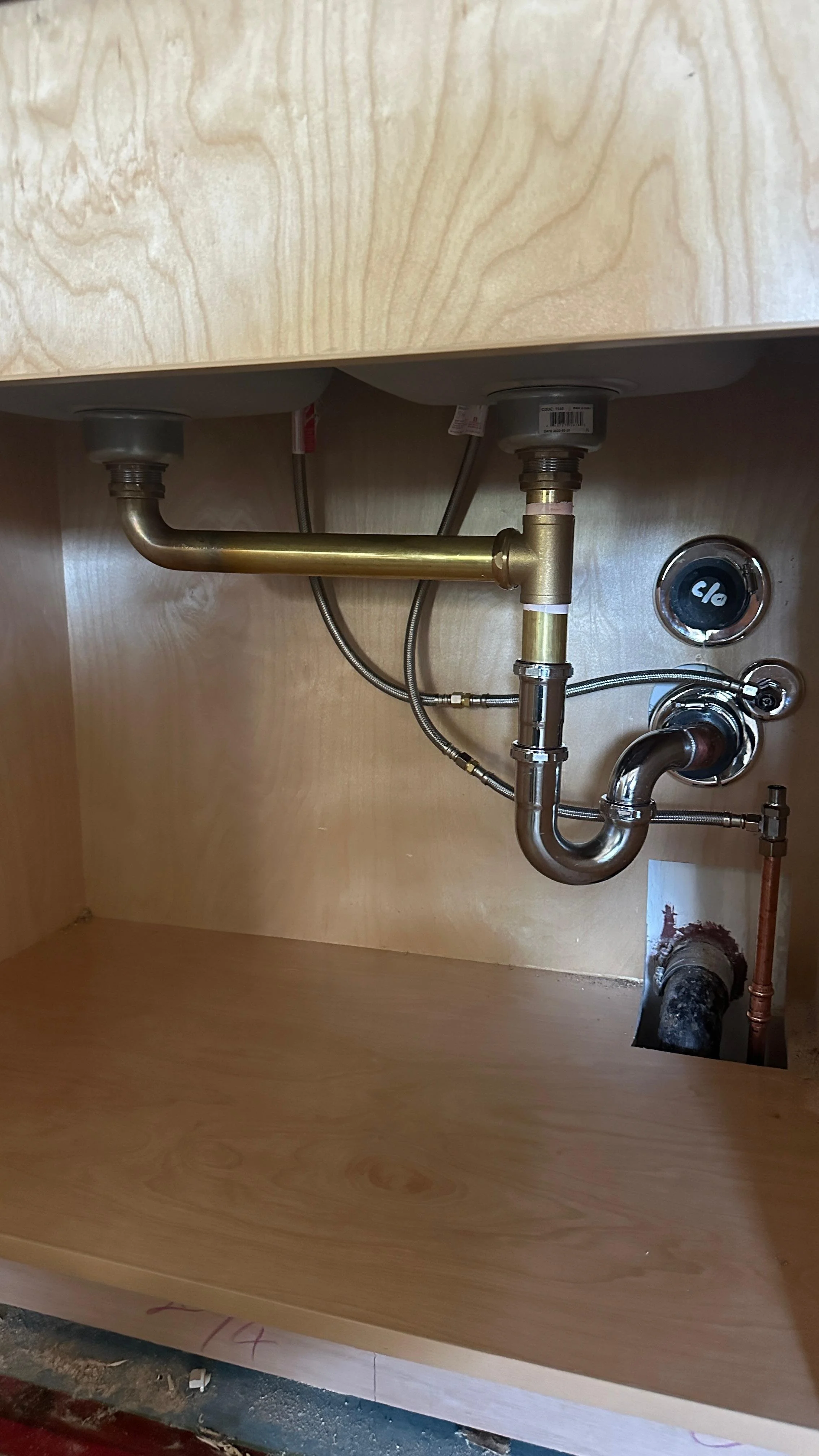 Under-sink plumbing pipes and connections inside a wooden cabinet, including metal pipes, flexible hoses, and valves.