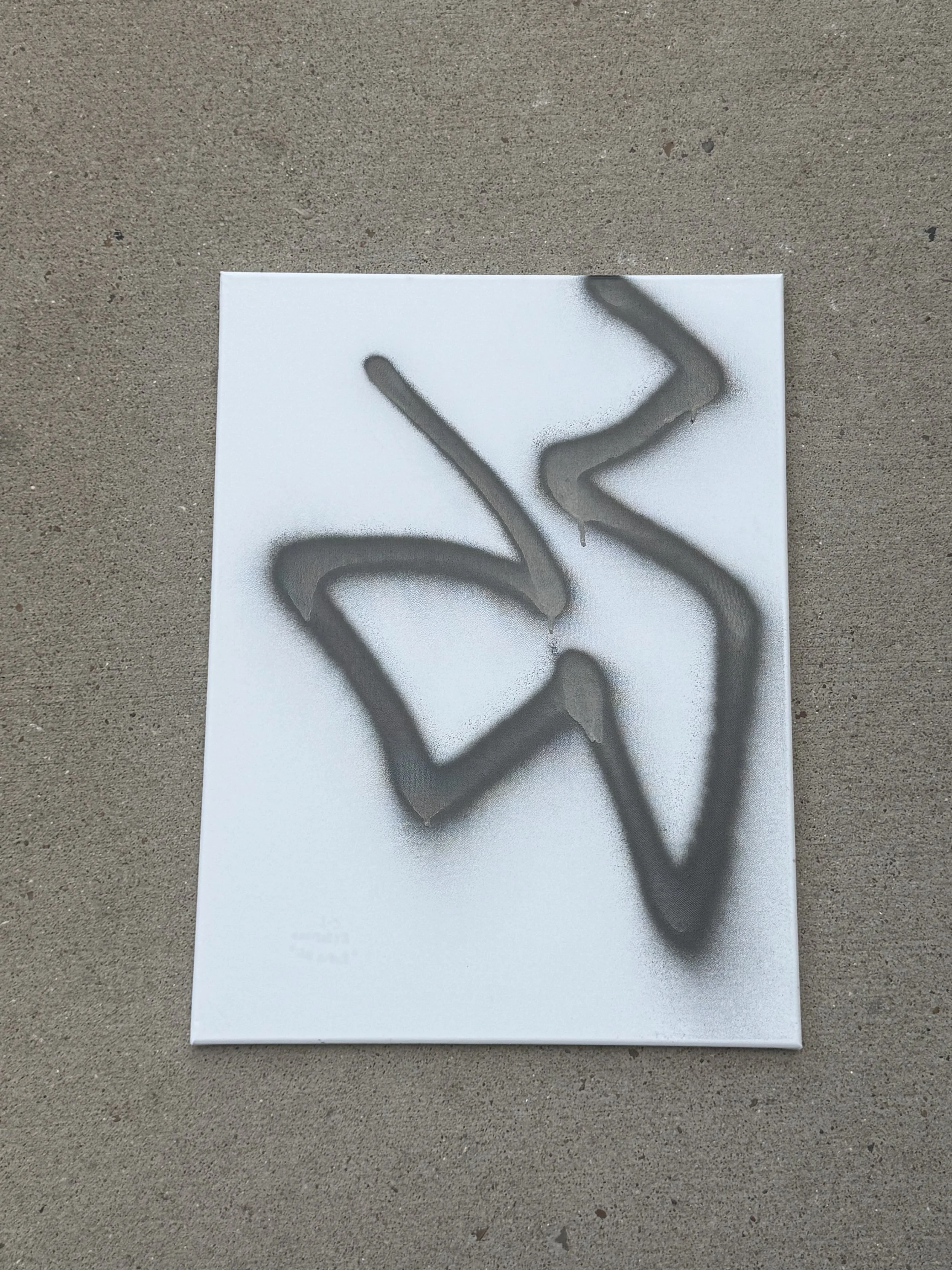 A white canvas with black spray paint graffiti forming an abstract shape.