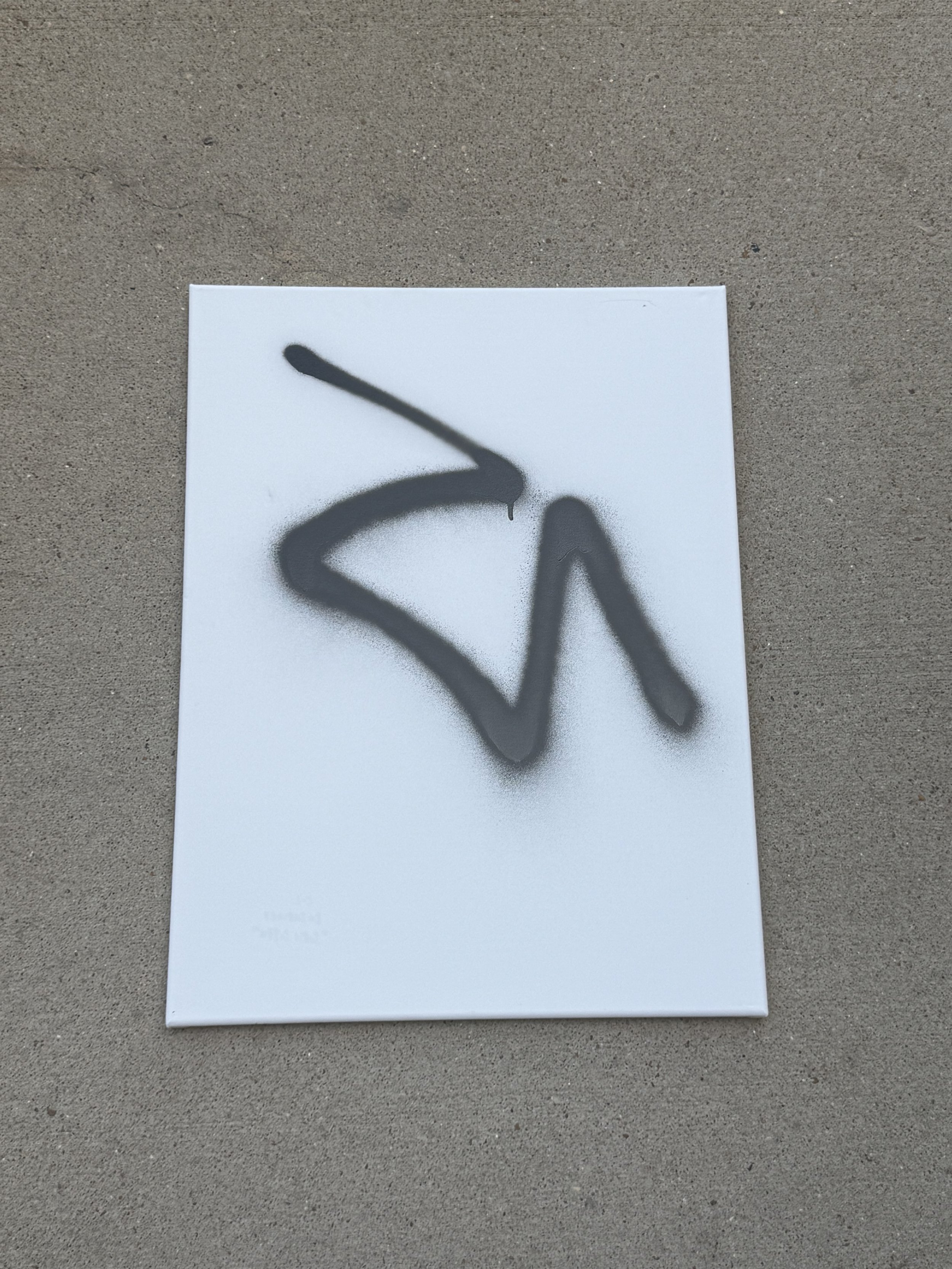 A white canvas with black spray paint graffiti forming an abstract shape.
