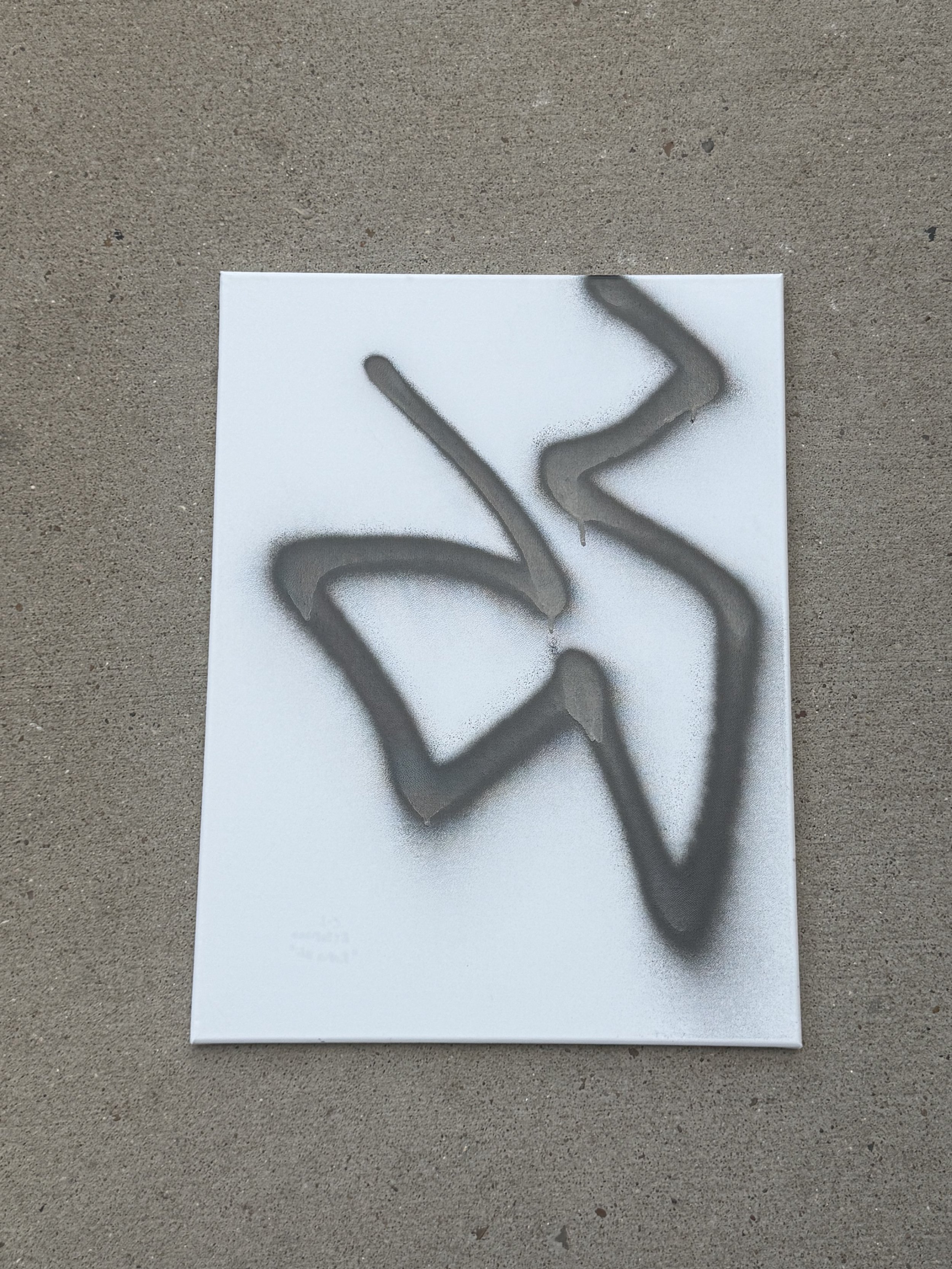 A white canvas with black spray paint graffiti forming an abstract shape.