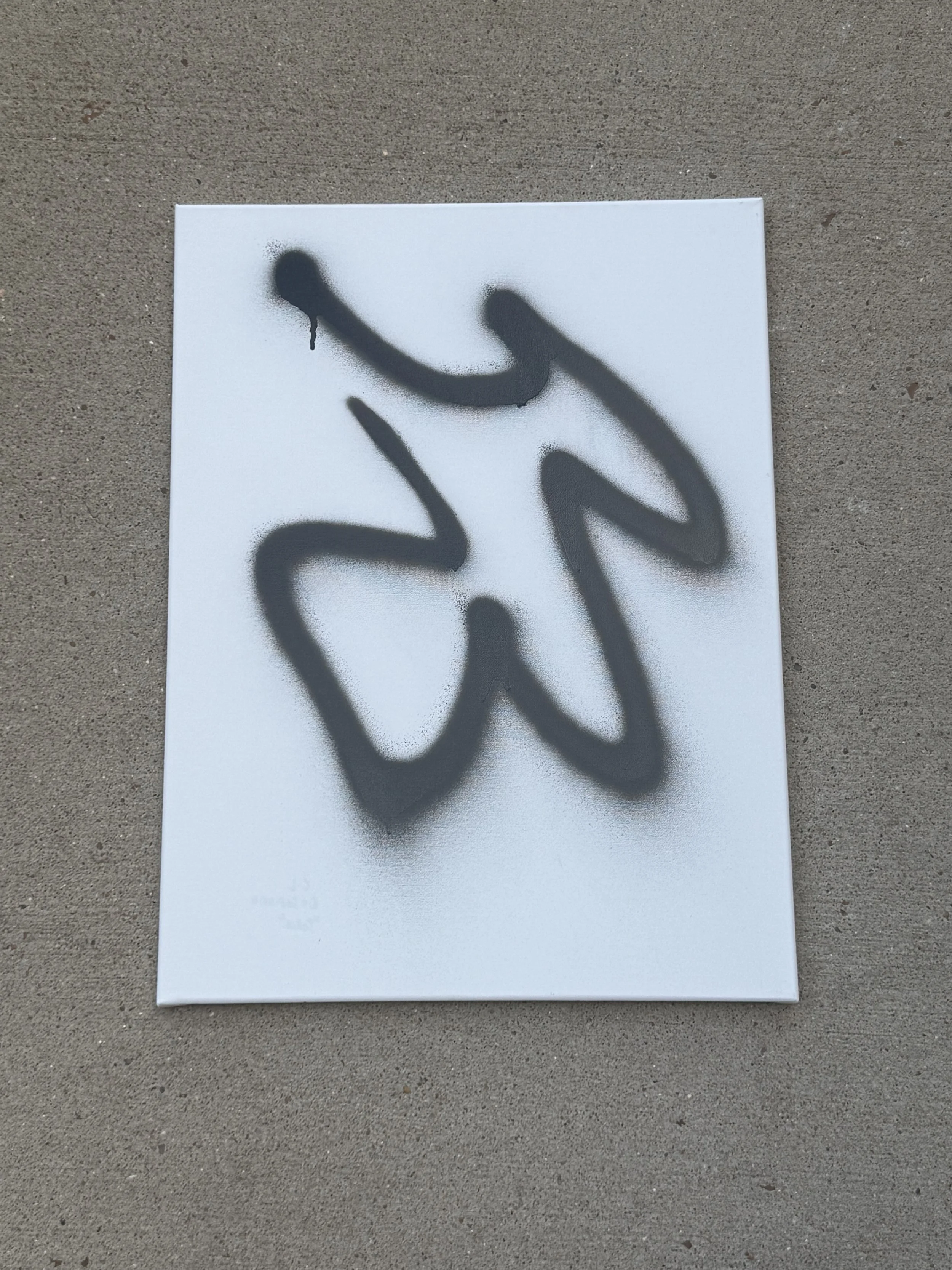 A white canvas with black spray paint graffiti forming an abstract shape.