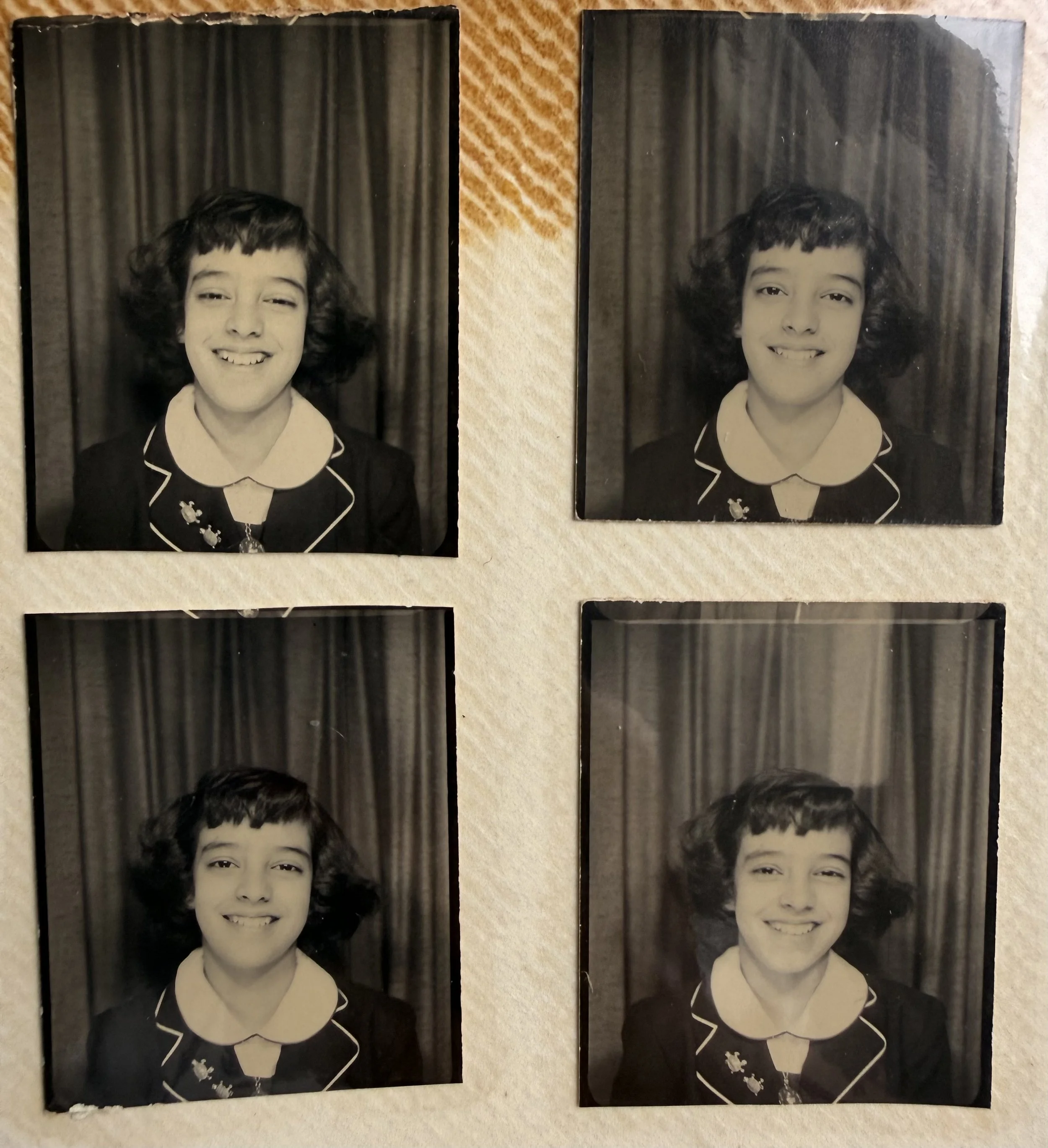 Fotografía antigua en blanco y negro de una niña con vestido oscuro y cabello rizado, sonriendo frente a cortinas.
