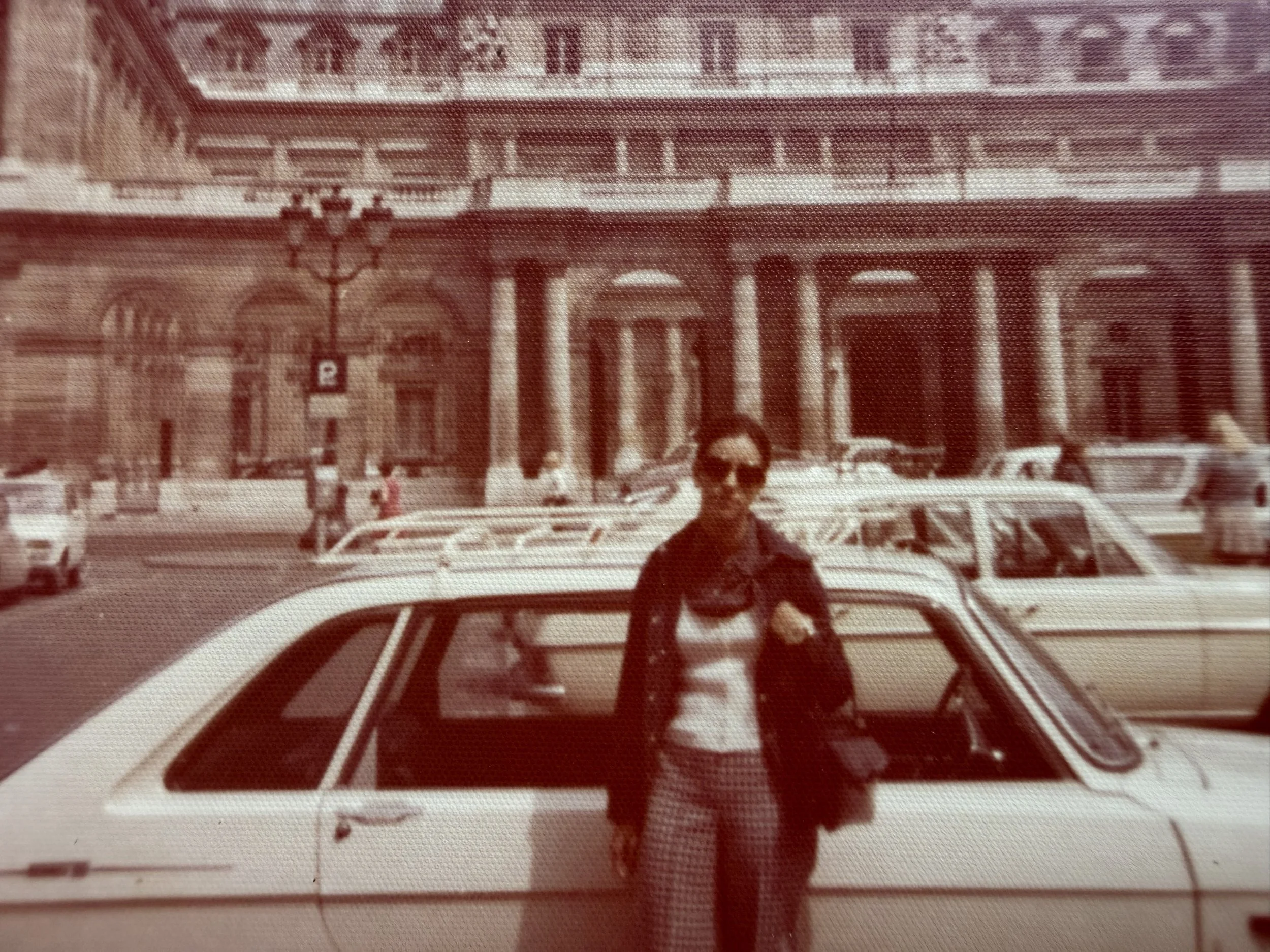 Foto de una mujer caminando por una calle con un edificio antiguo en el fondo, con letras grandes que dicen 'BANK' en la parte superior del edificio y un cartel con la letra 'P' en la esquina de la acera.