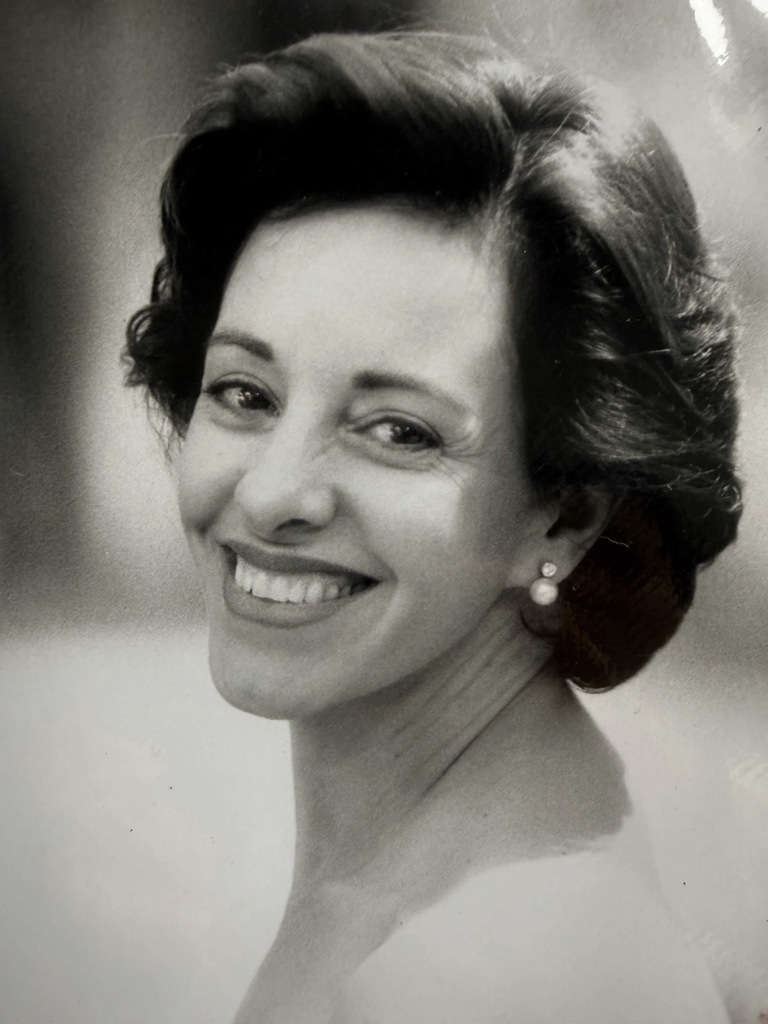 Retrato en blanco y negro de una mujer con cabello corto y rizado, sonriendo y usando pendientes de perlas.