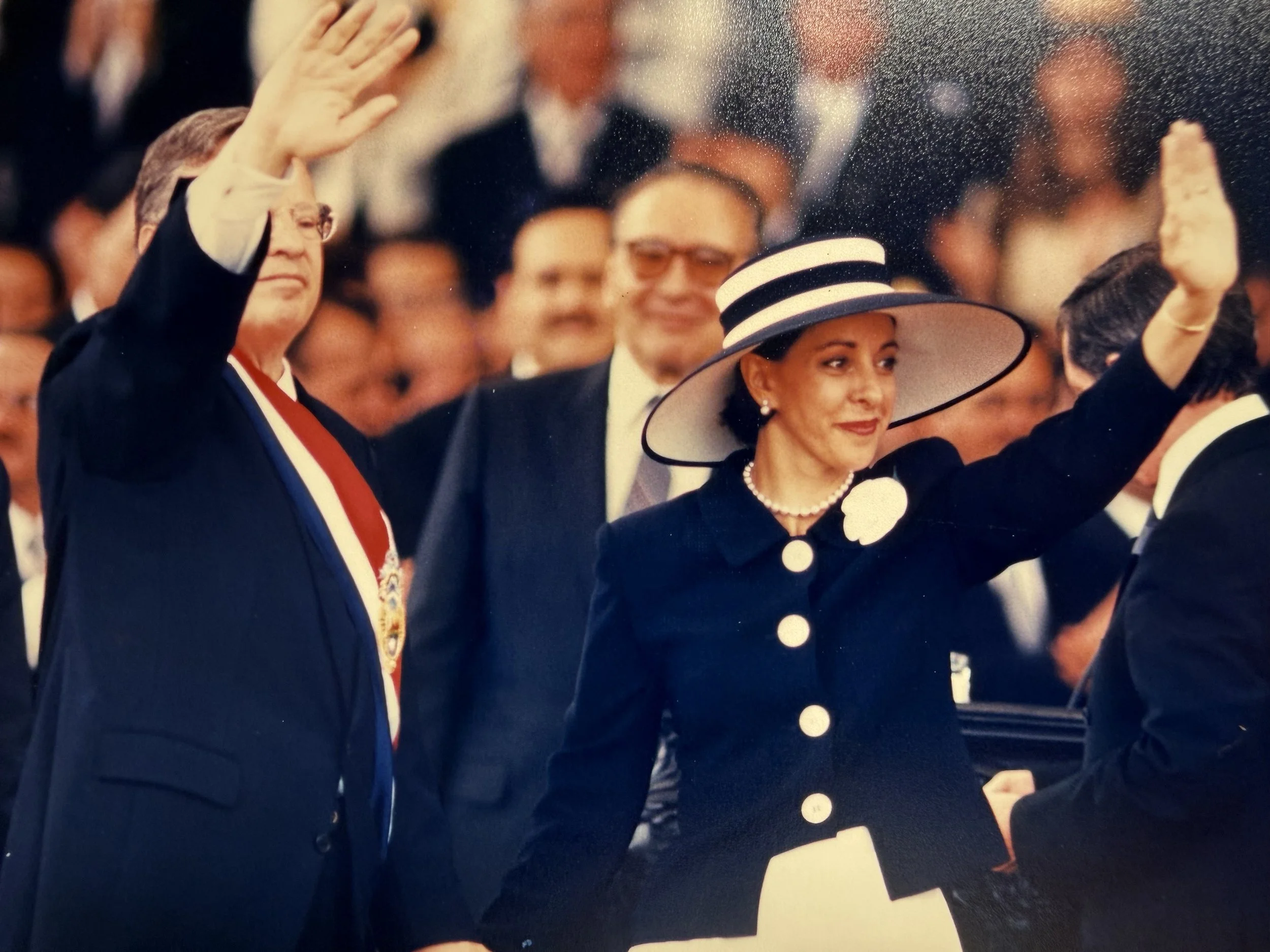 Registro del acto en una ceremonia formal con varias personas vestidas elegantemente, levantando la mano en señal de saludo o juramento.