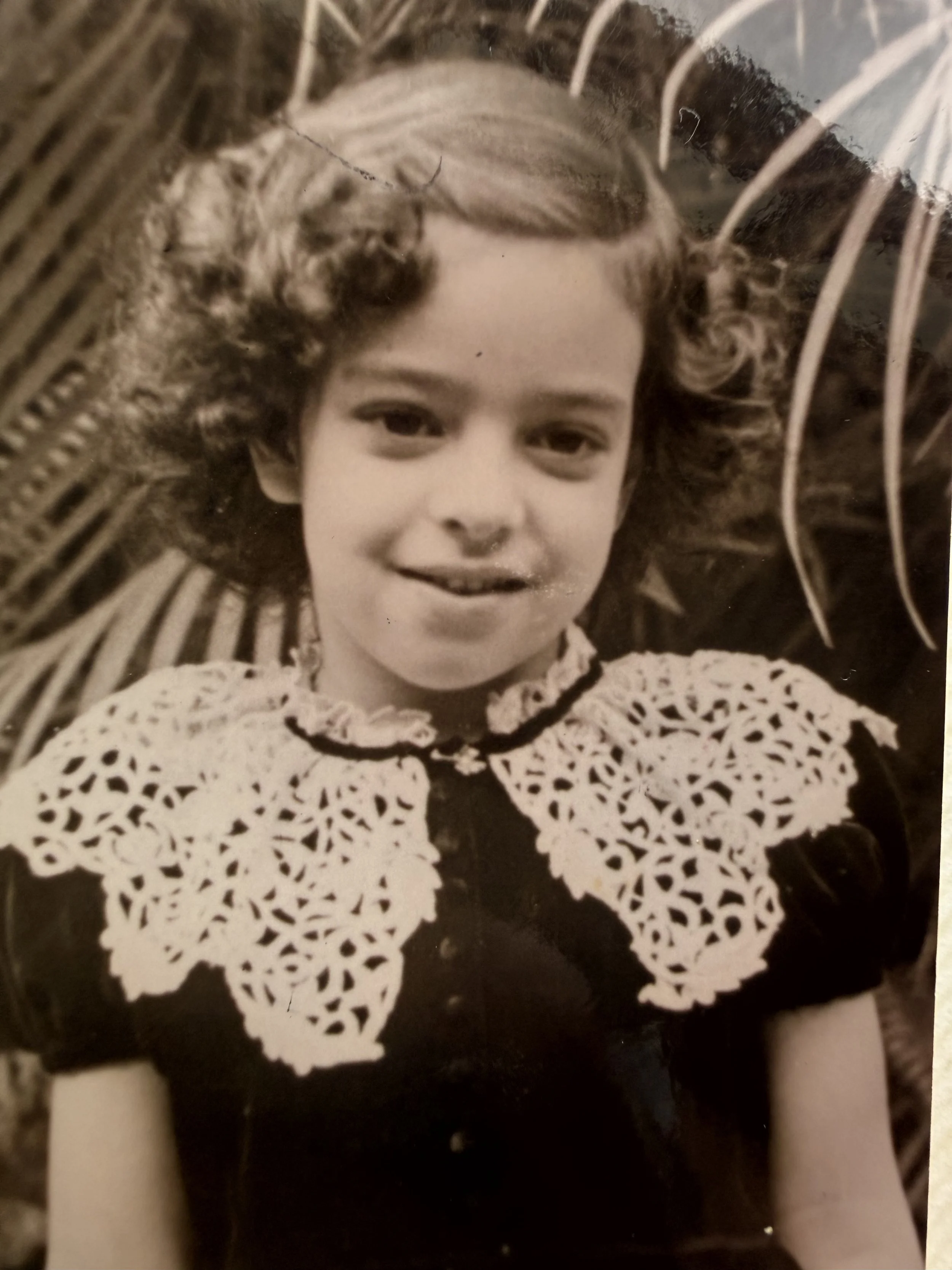 Retrato en blanco y negro de una niña sonriendo, con cabello rizado y vestida con un top con encaje.
