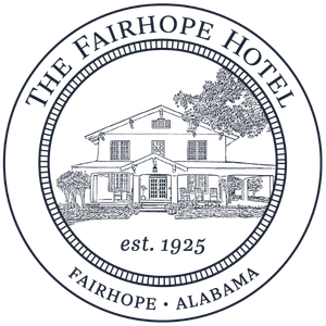 A circular logo for The Fairhope Hotel in Fairhope, Alabama, established in 1925, featuring an illustration of a building with a porch, trees, and decorative elements.