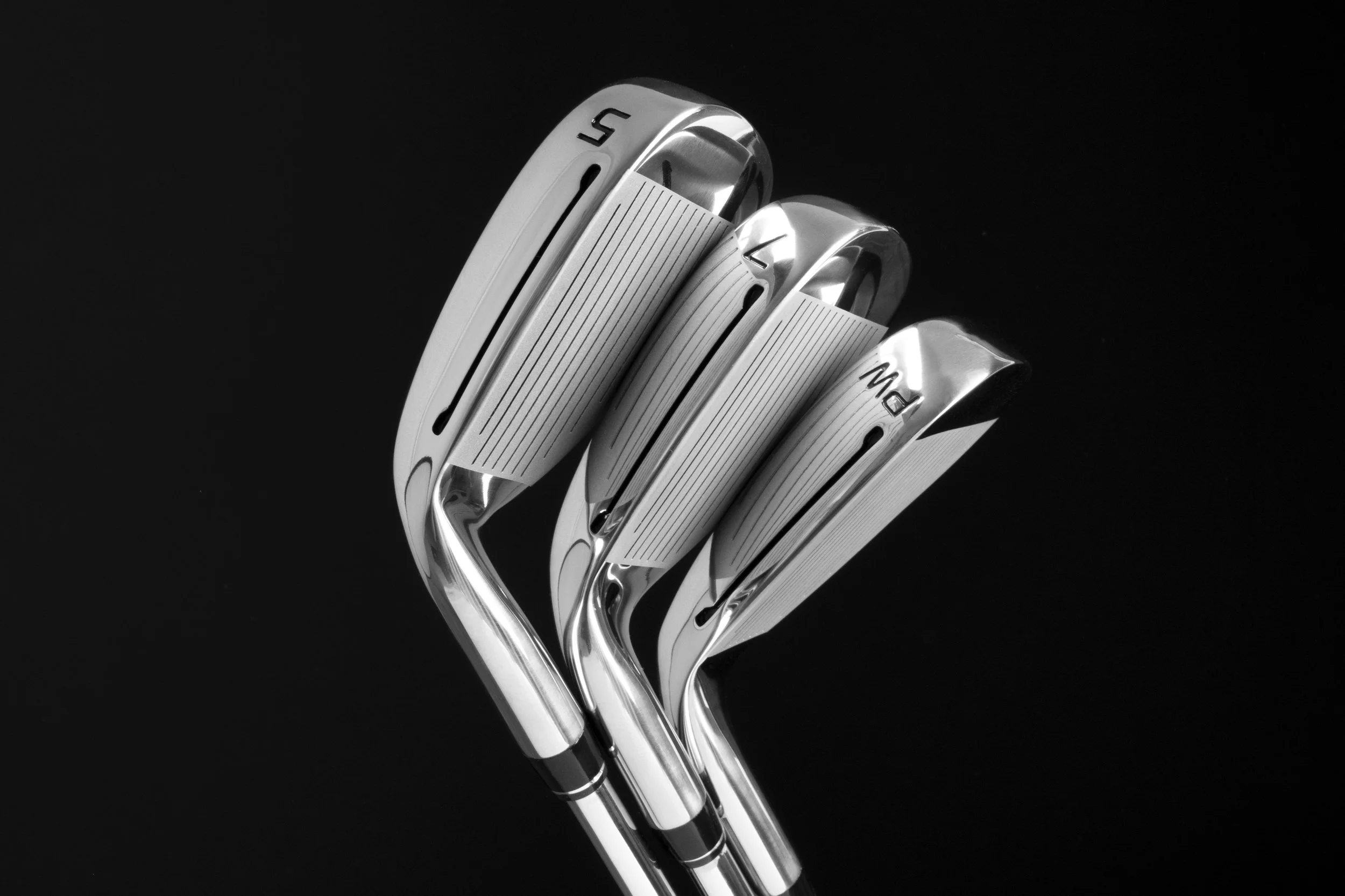 Close-up of four shiny golf clubs with metallic heads against a black background.