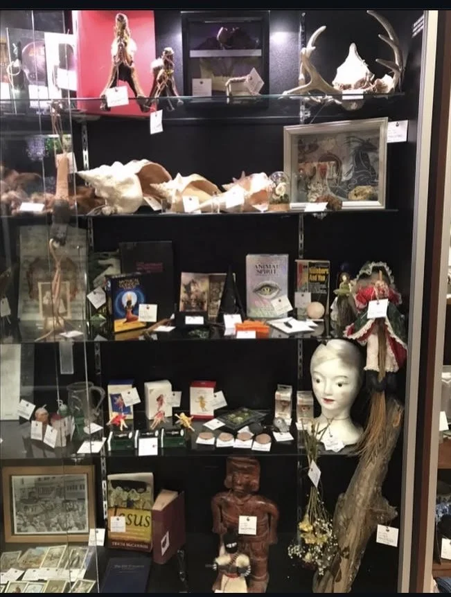 A black display cabinet filled with various collectibles, including dolls, books, artwork, and decorative items in a store.