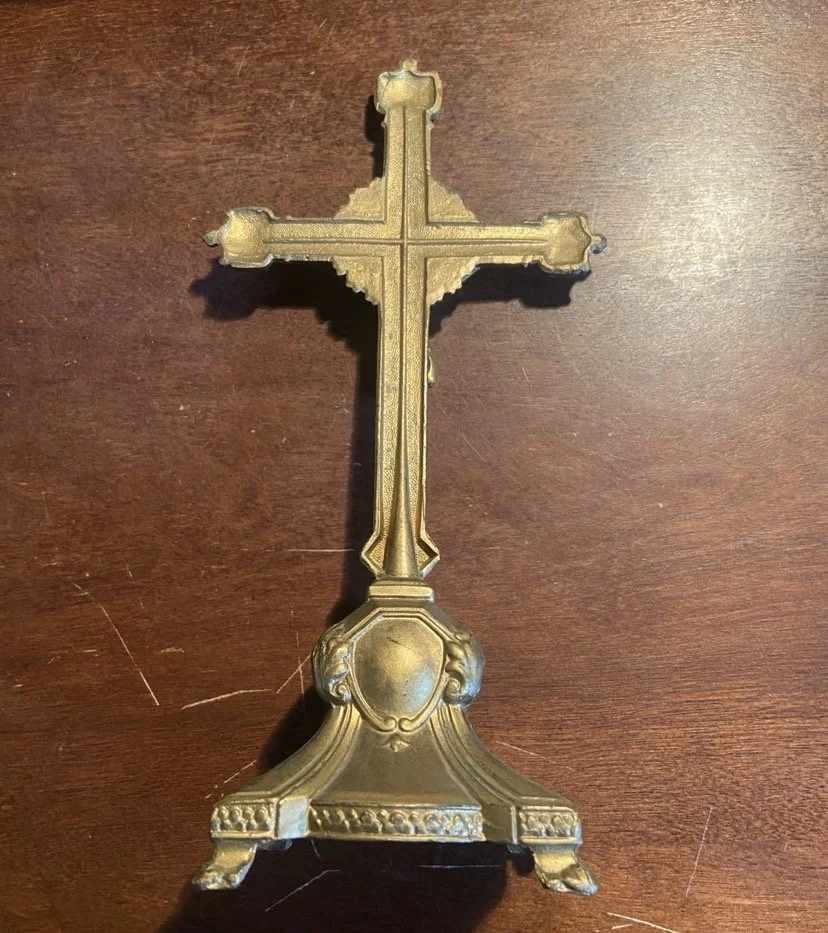An ornate brass or gold-colored standing cross with decorative details, placed on a wooden surface.