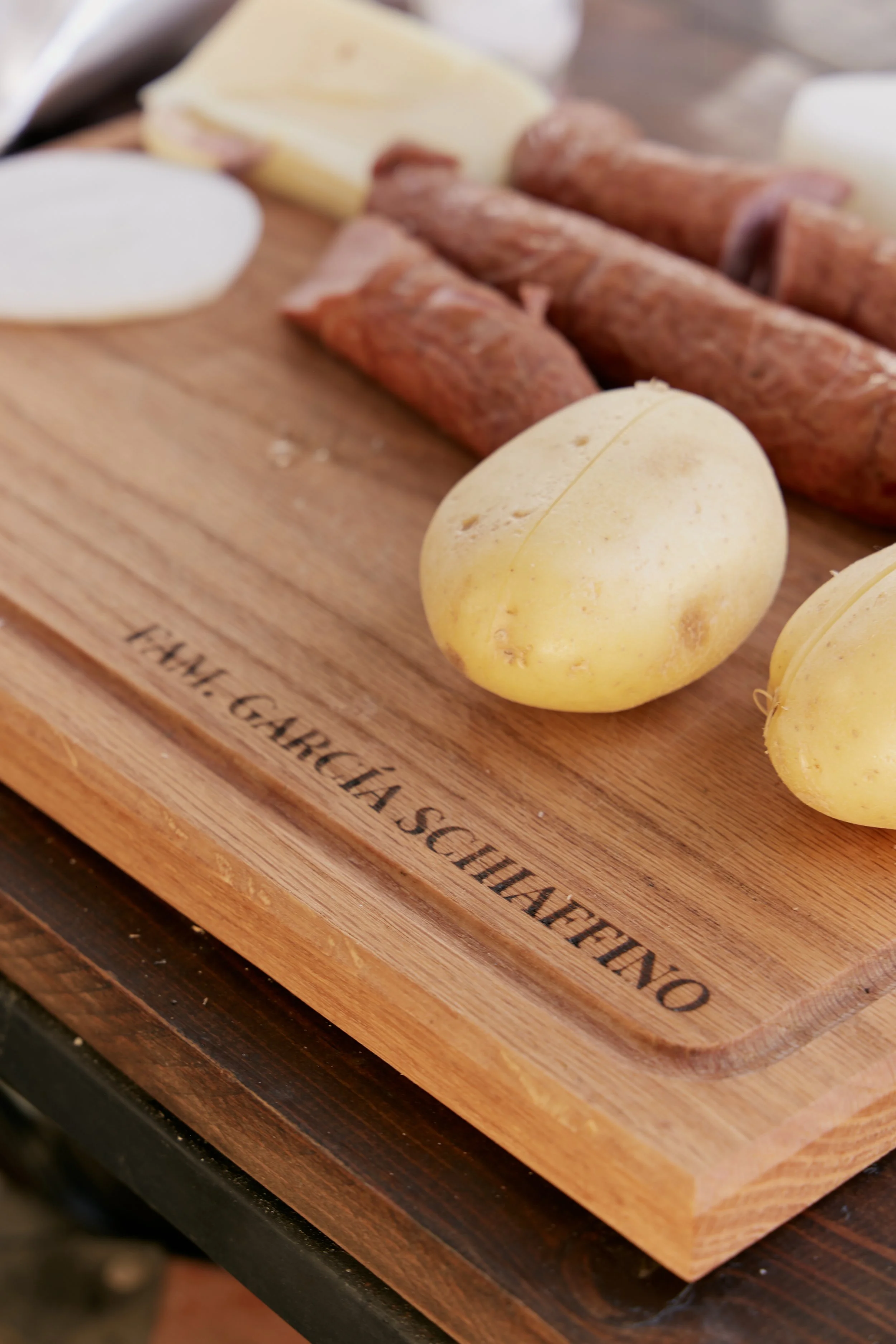 Tabla de madera con diferentes tipos de queso y embutidos, algunos en forma de bolas y otros en tiras enrolladas.