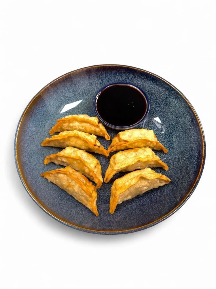 Six fried dumplings arranged on a dark blue plate with a small bowl of soy sauce in the center.