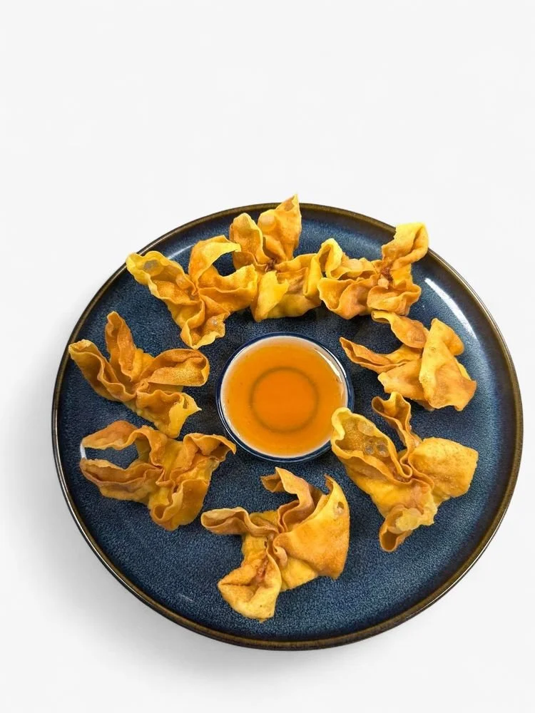 A black plate with fried wontons arranged around a small bowl of dipping sauce on a white background.
