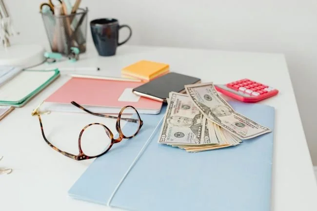 desk top showing reading glasses, cash, calculator, coffee representing what is a Roth IRA