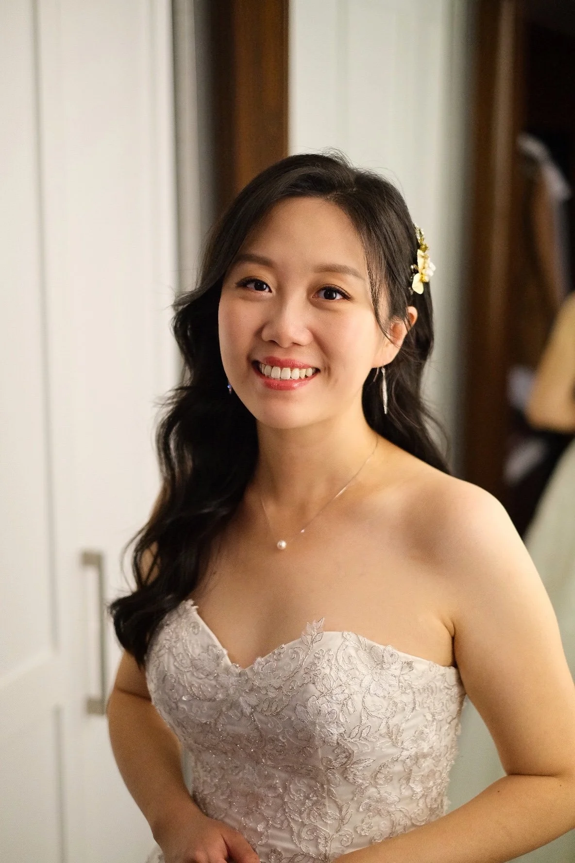 A young woman with long, dark hair smiling in a white lace strapless dress.