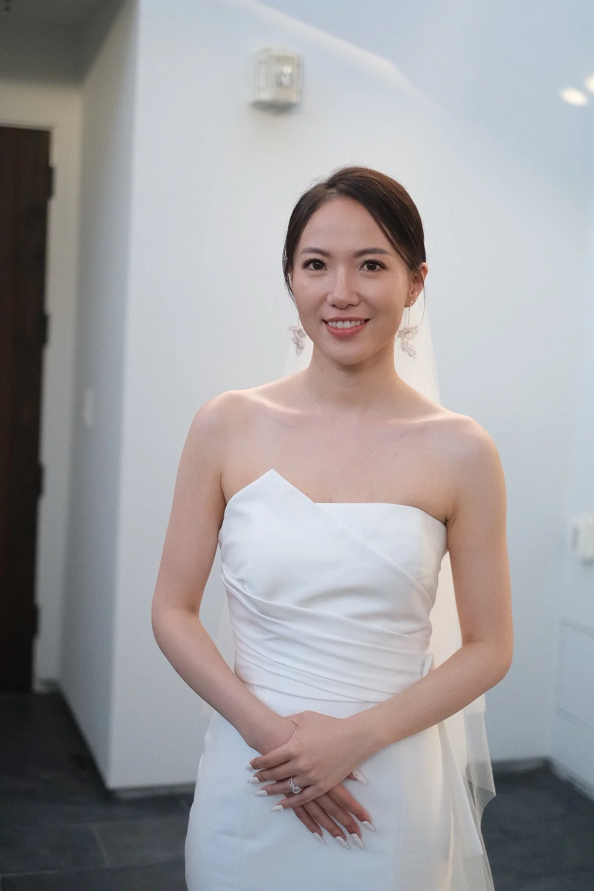 A woman in a strapless white wedding dress smiling indoors.