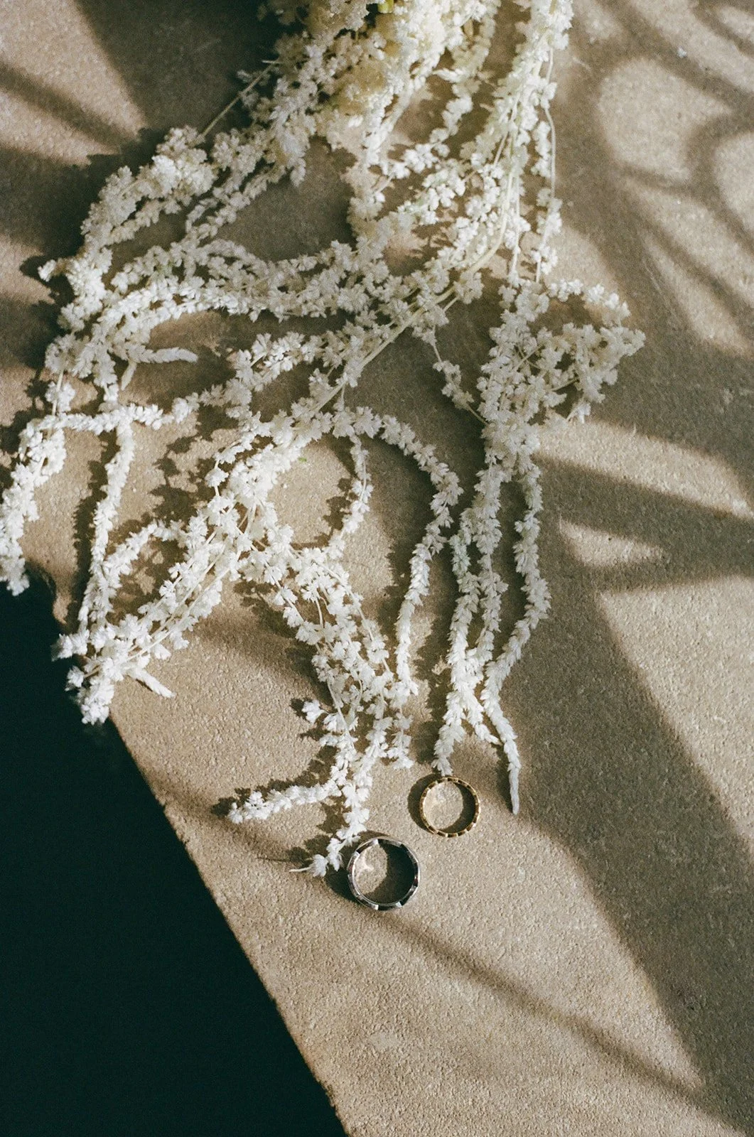 A beige fabric surface with white decorative branches and two rings, one gold and one silver, resting on the branches.