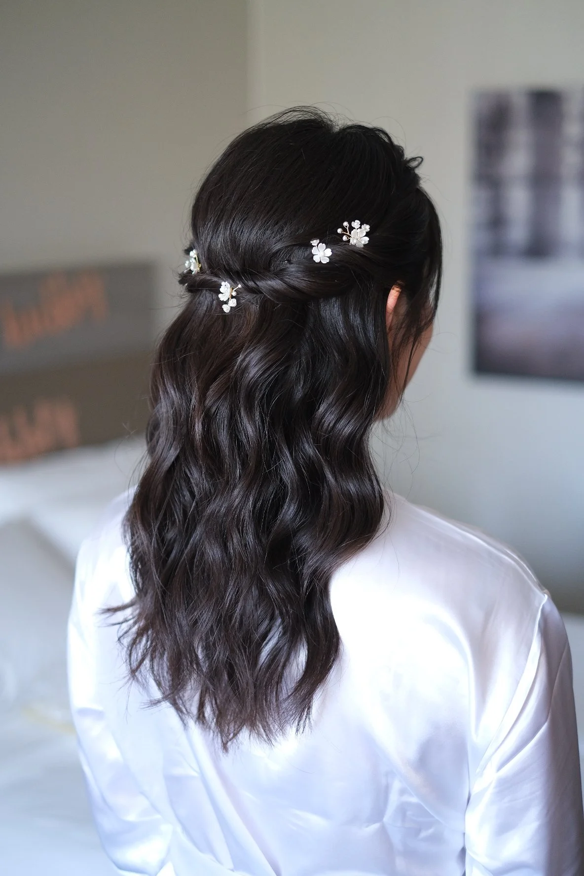 Woman with wavy dark hair styled in a half-up, half-down hairstyle decorated with small white floral hair accessories.