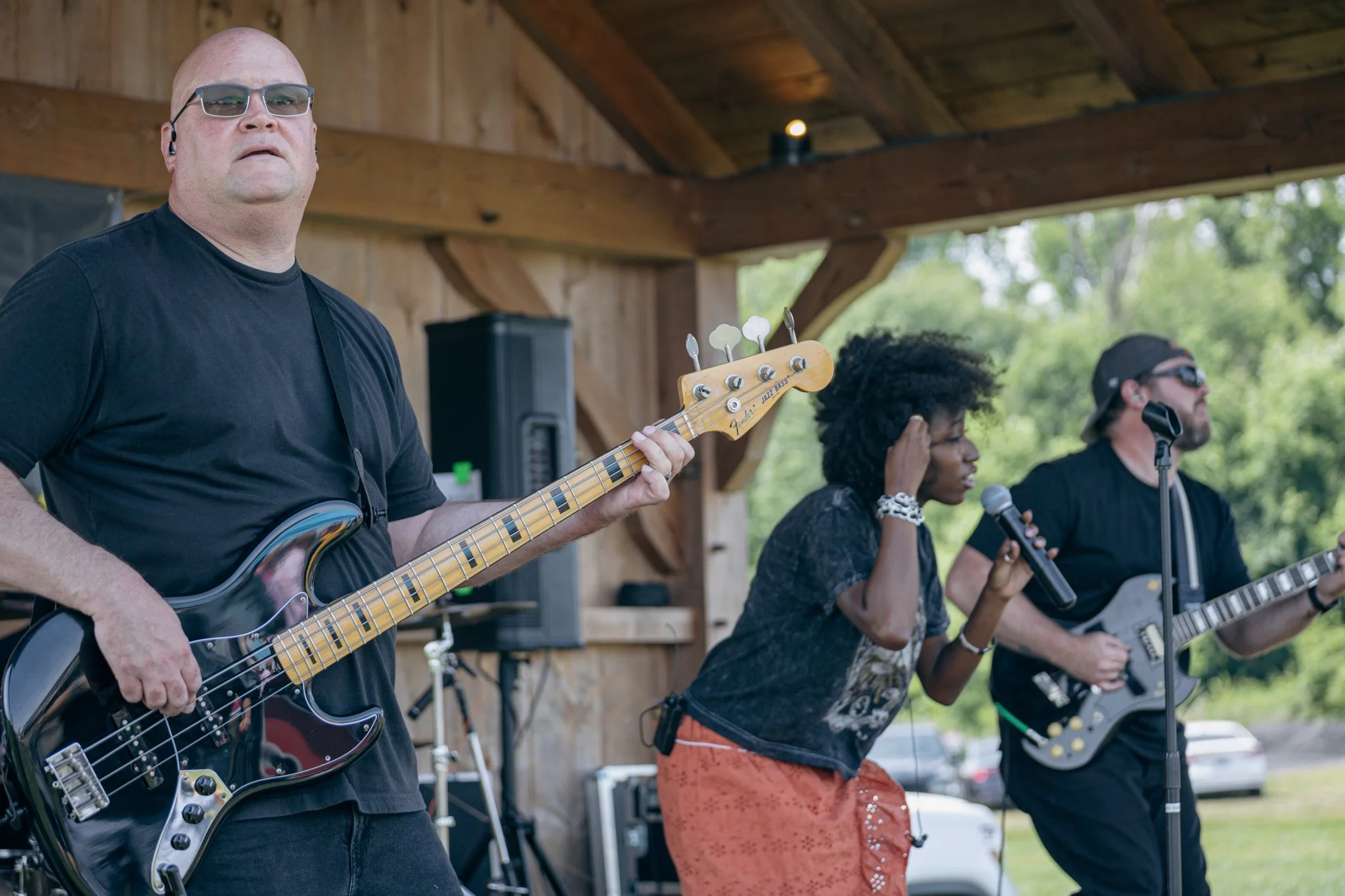 A group of musicians performing outdoors under a wooden pavilion, playing guitars and singing.