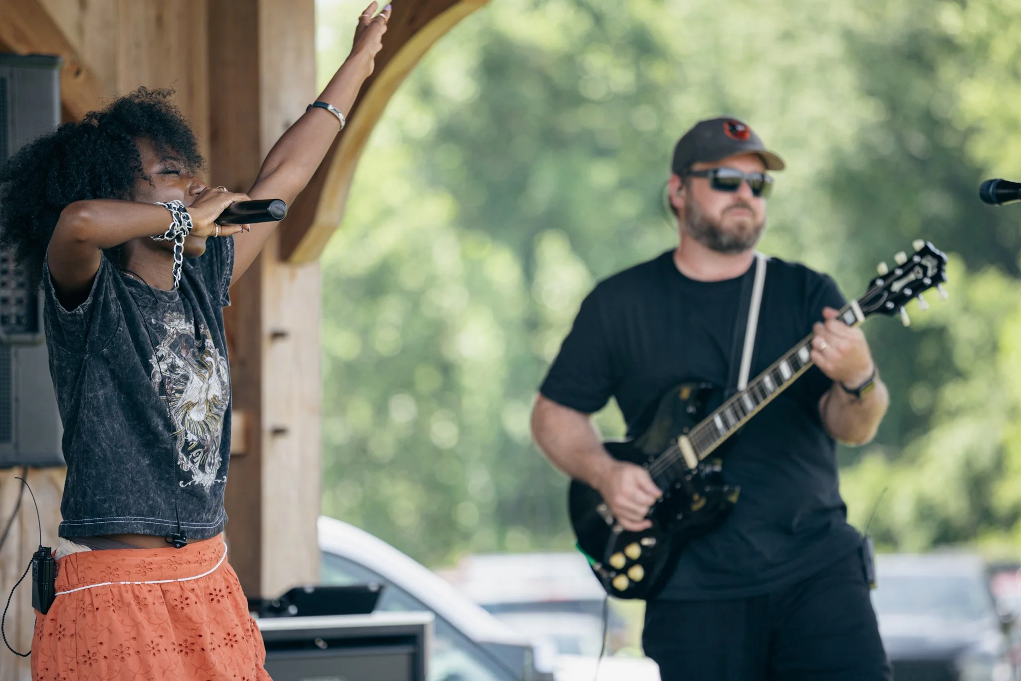 A woman singing into a microphone and a man playing a guitar outdoors.