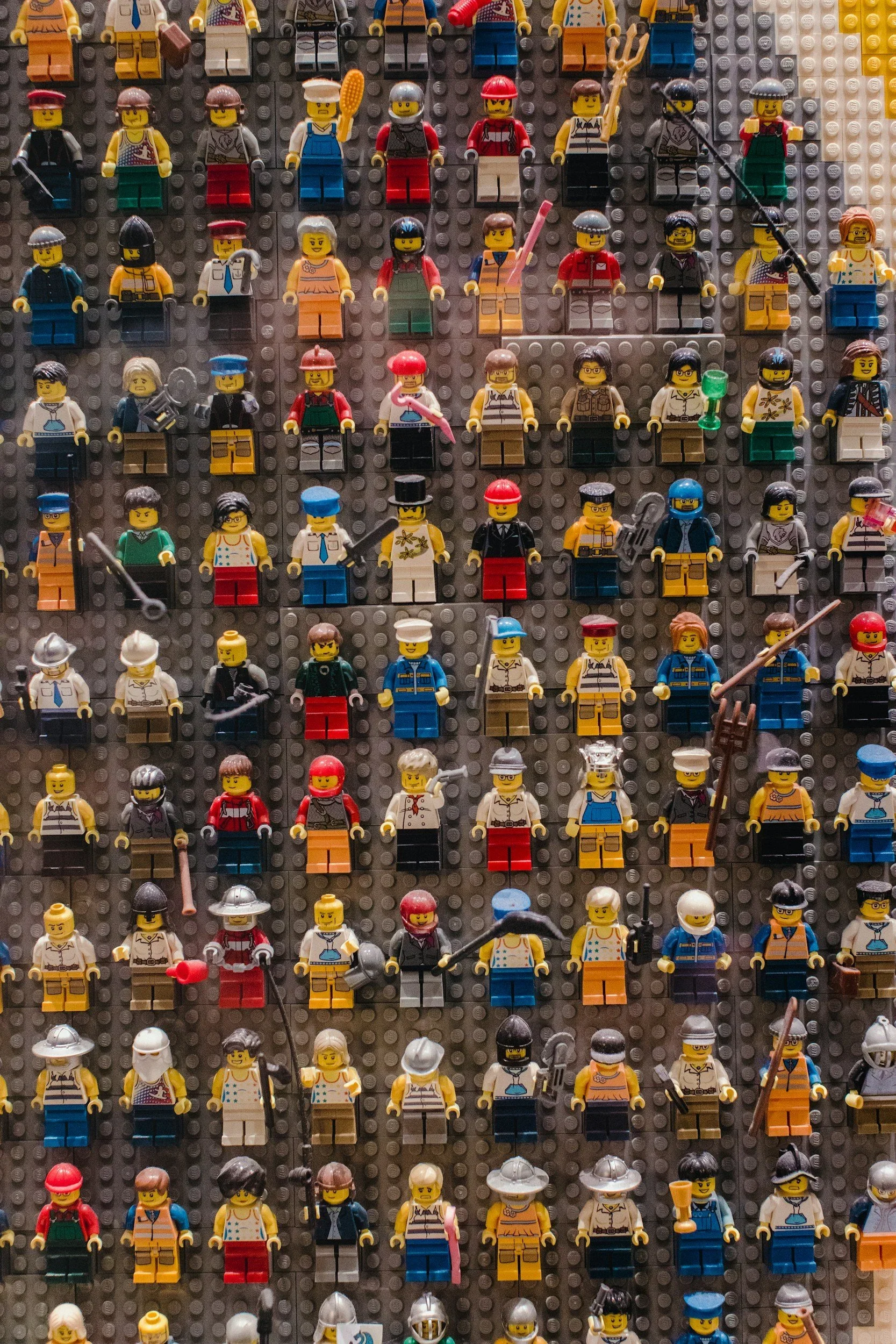 A display of numerous LEGO minifigures arranged on a gray baseplate, each dressed in various costumes and accessories representing different characters and professions.