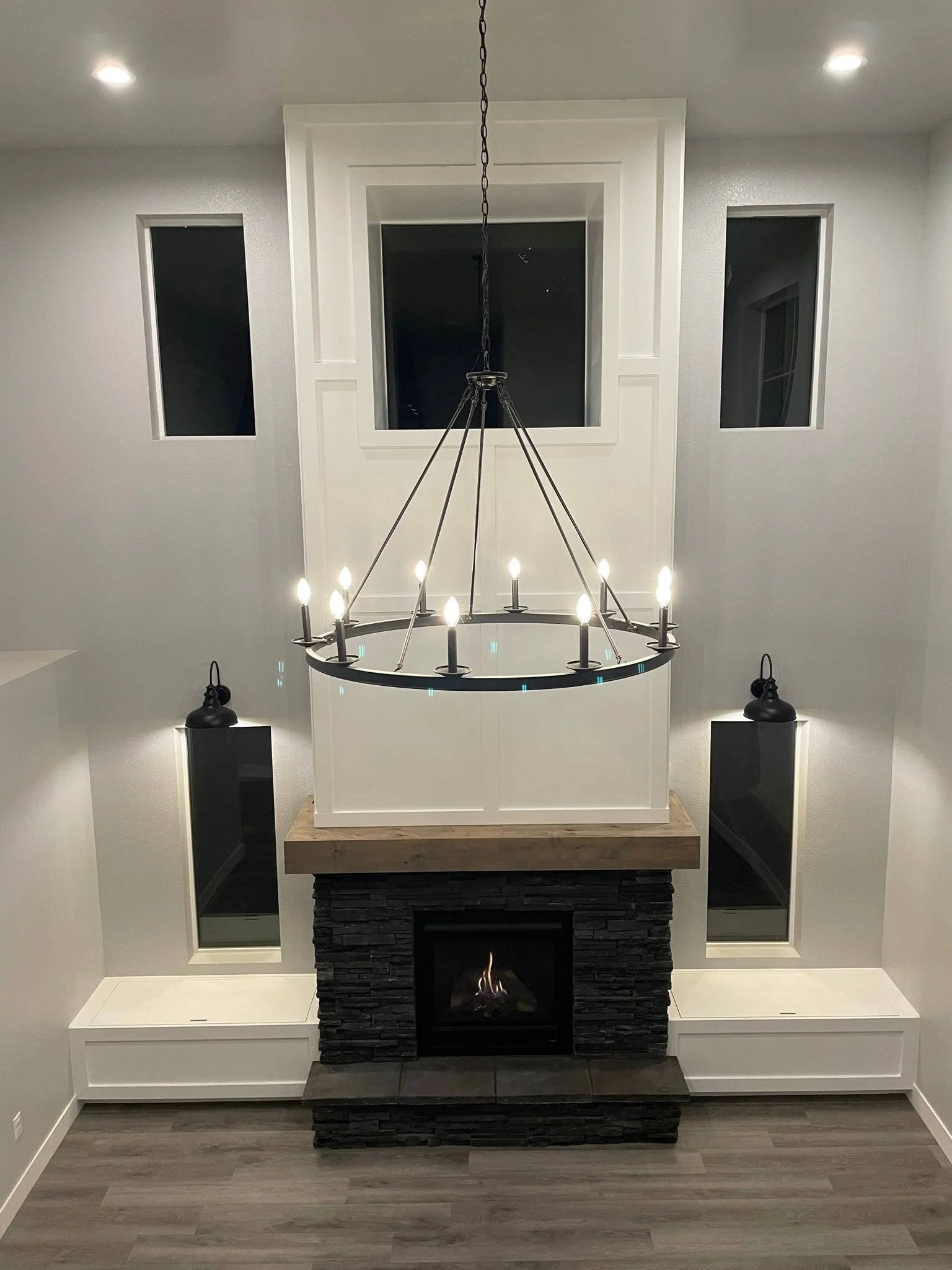 Newly framed out and installed fireplace with custom benches, mantle, and stone. Custom lighting and chandelier installed in a living room.