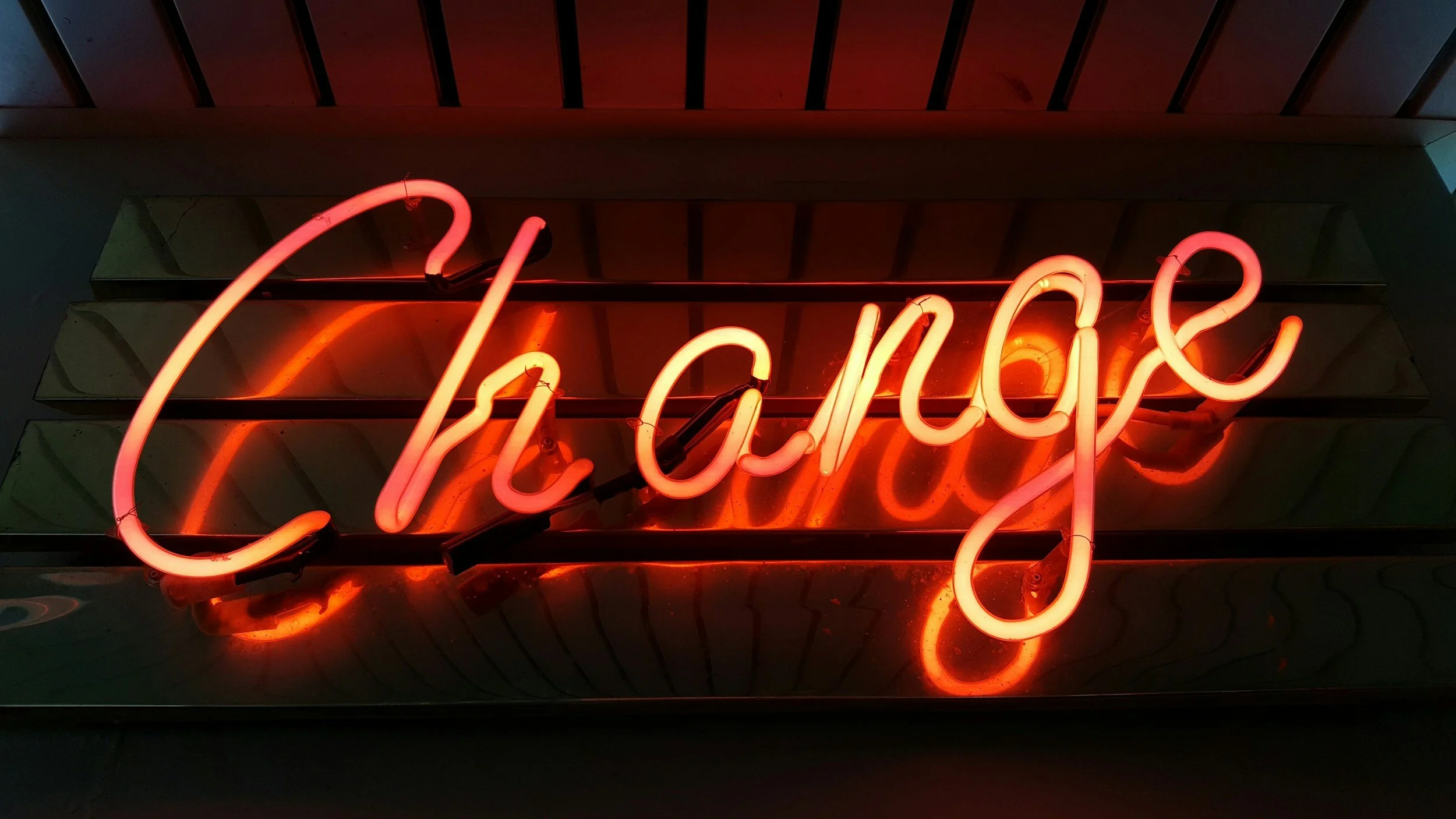 A neon sign spelling out the word 'change' in cursive, illuminated in red and pink colors.