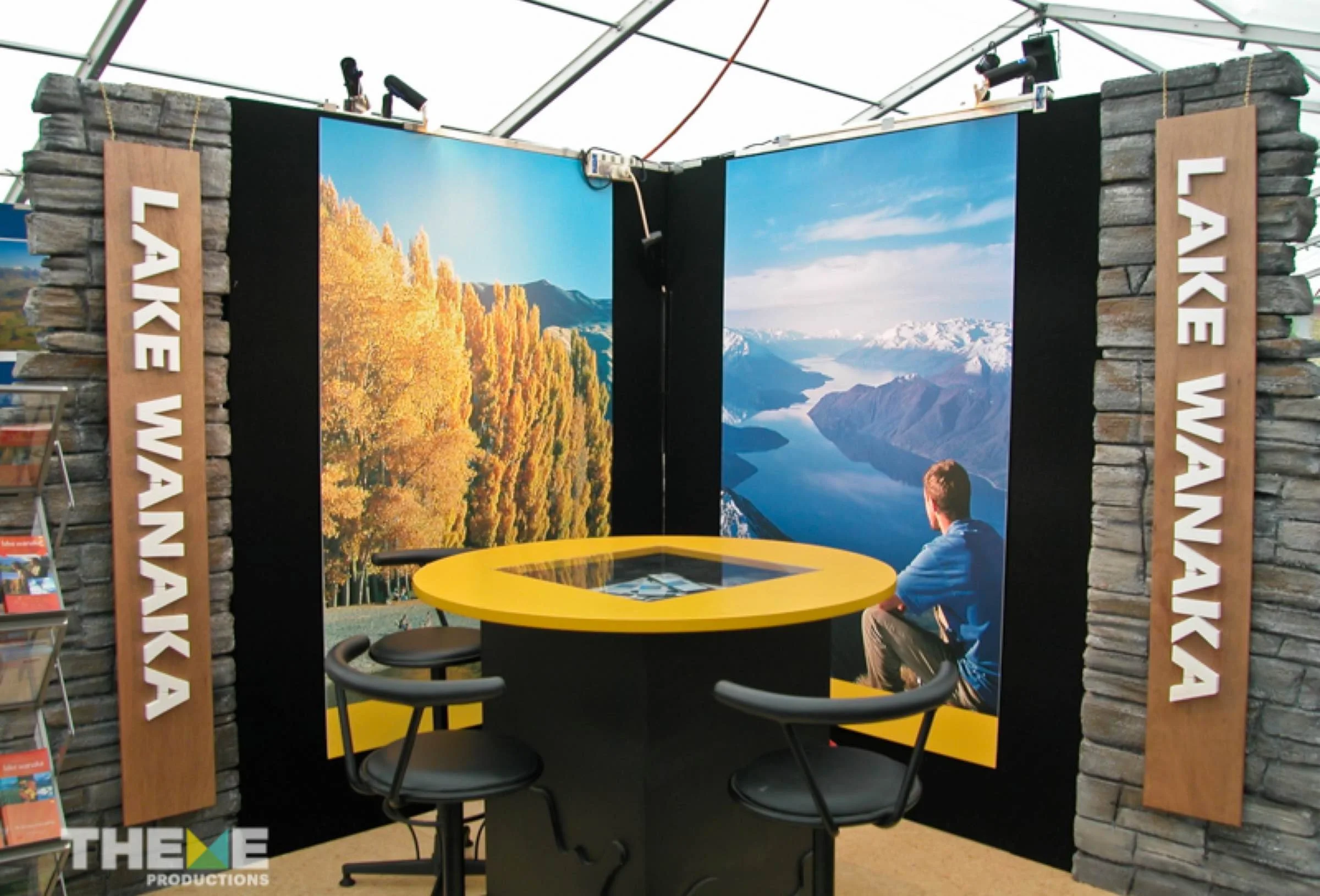 Exhibit booth with two large scenic landscape photos of mountains and lakes, with 'LAKE WANA' signs on stone columns on either side.