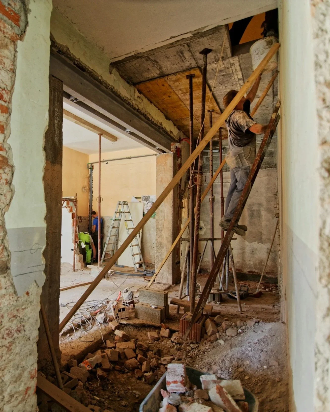 Construction workers demolishing or renovating an interior building, with debris and scaffolding.