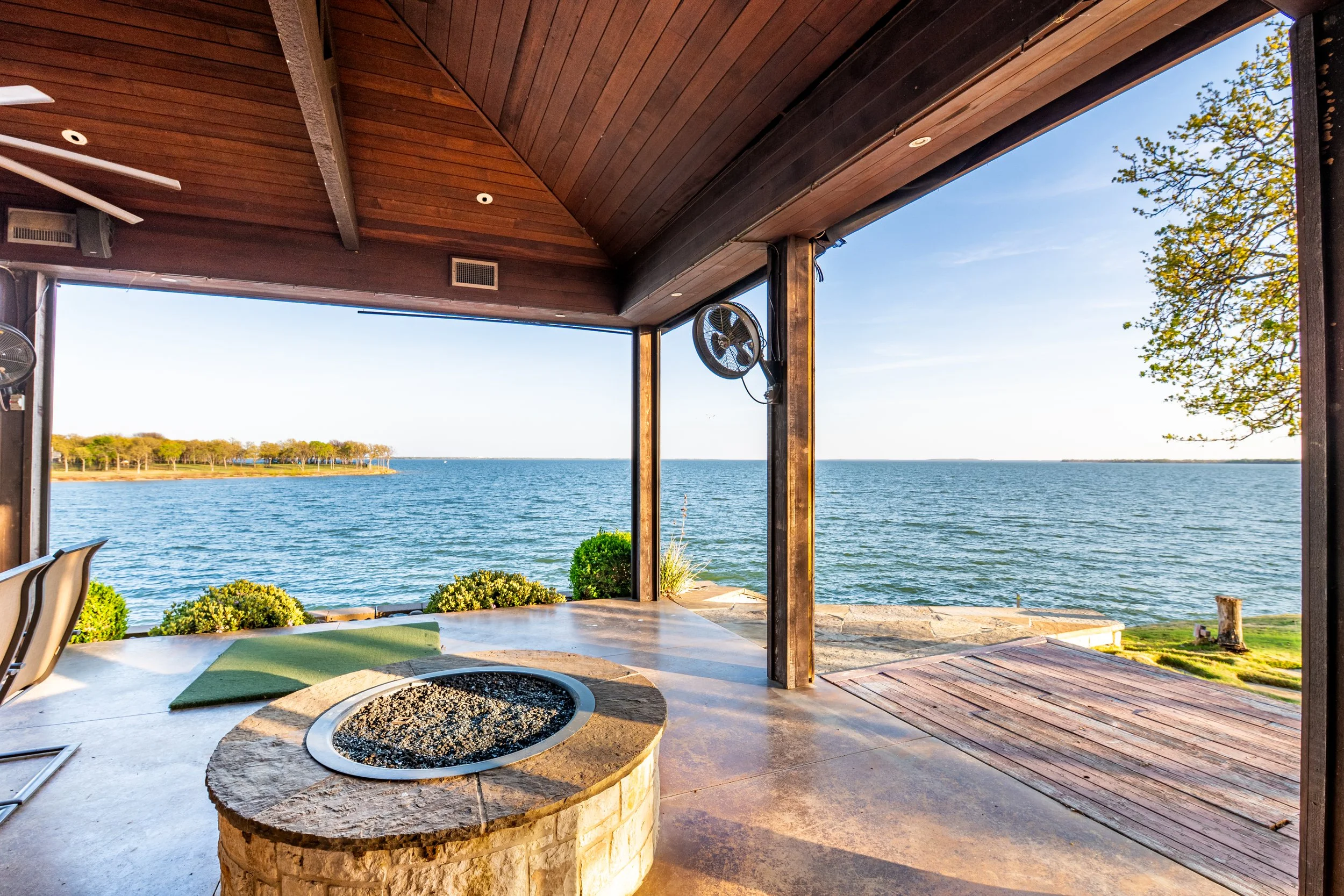 Outdoor patio with a view of a lake, wooden ceiling, ceiling fans, and landscaped plants.