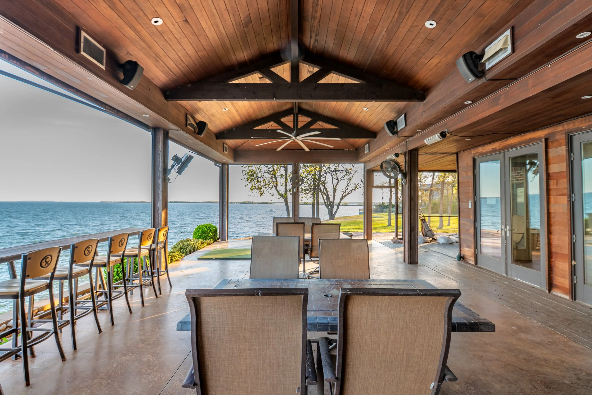 Covered outdoor patio with wooden ceiling, ceiling fans, and views of water and trees in the background.