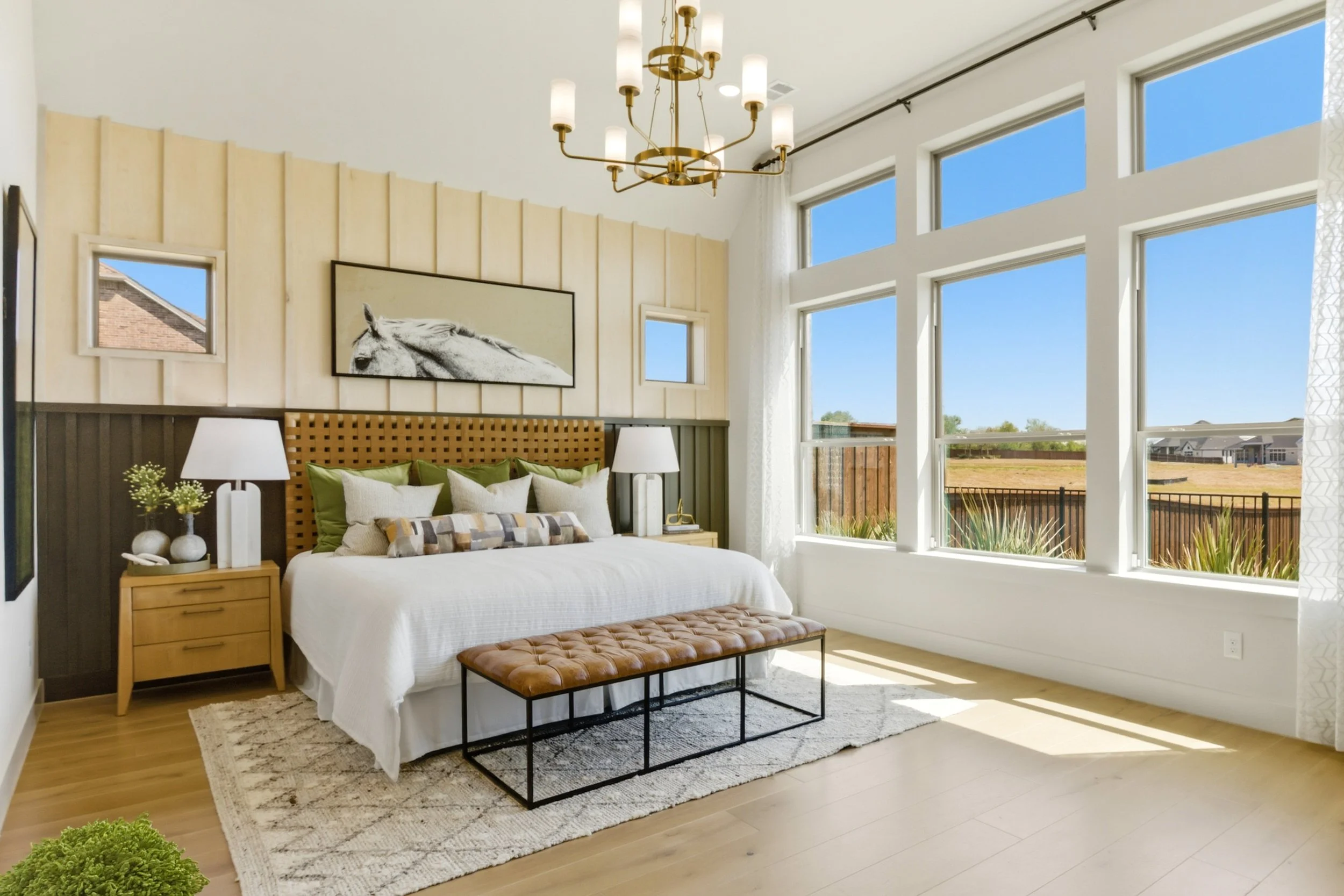 Bedroom with large windows, a bed with white bedding and green pillows, artwork of a horse, and modern furniture.