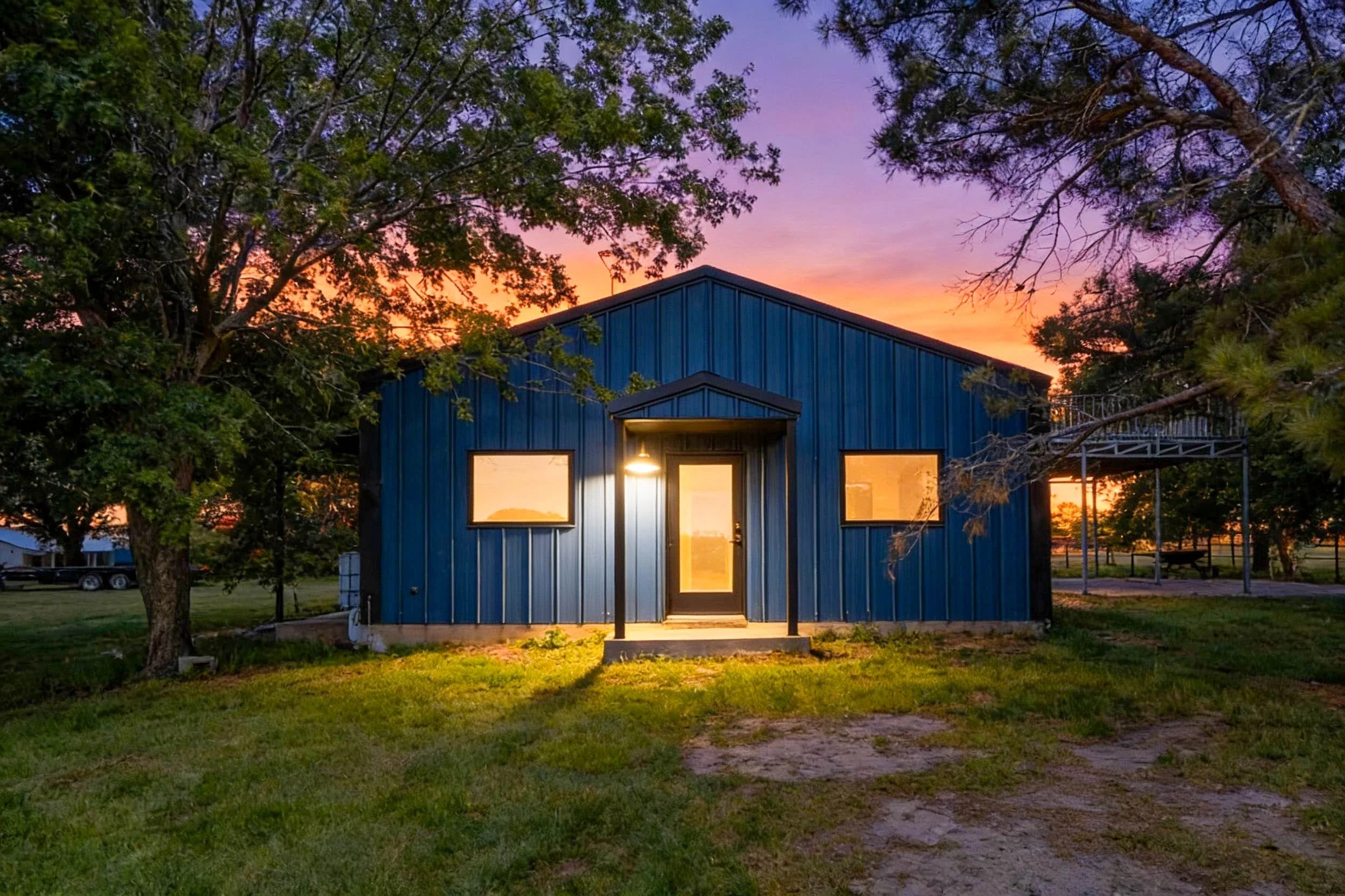 A blue building with large windows at sunset, surrounded by green trees and grass.