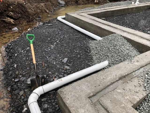 Travaux de construction avec des tuyaux en PVC, du gravier et une pelle à côté d'une structure en béton.